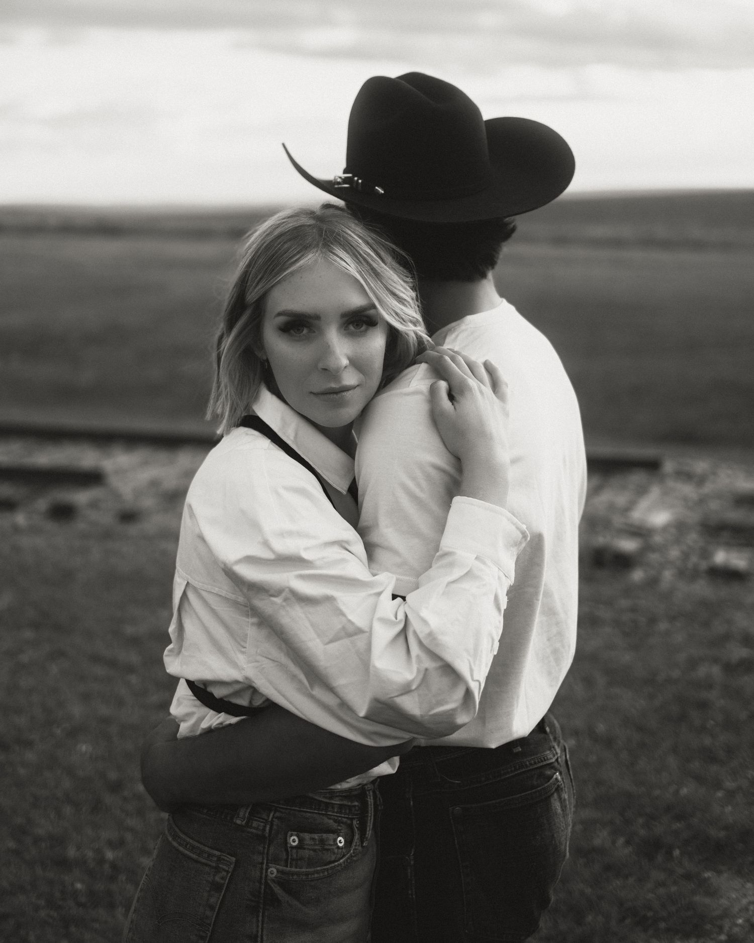 Black and white romantic western-themed couple portraits in an open field.