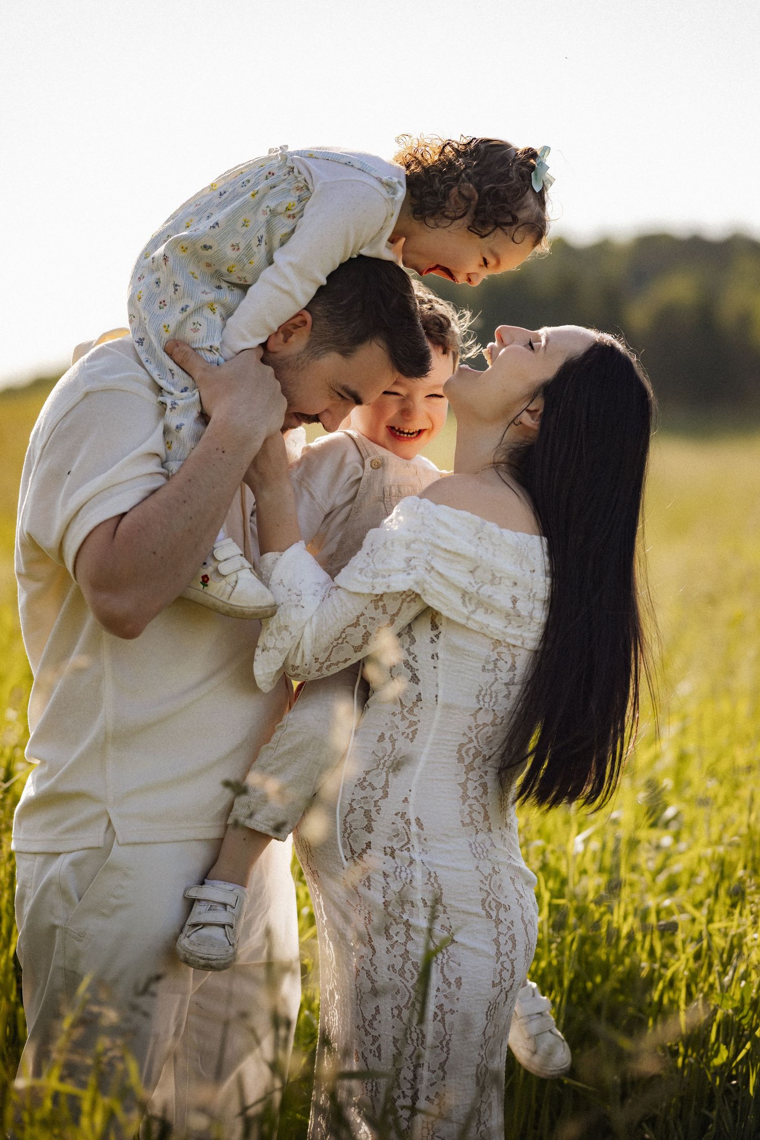 A touching family moment captured in a sunlit field with white outfits.