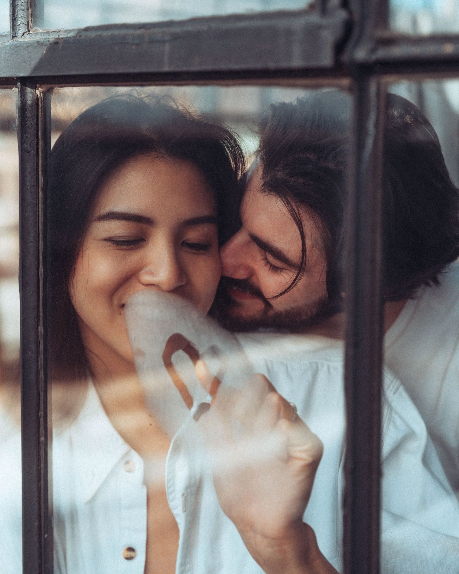 Intimate couple photoshoot through window panes with soft natural light.