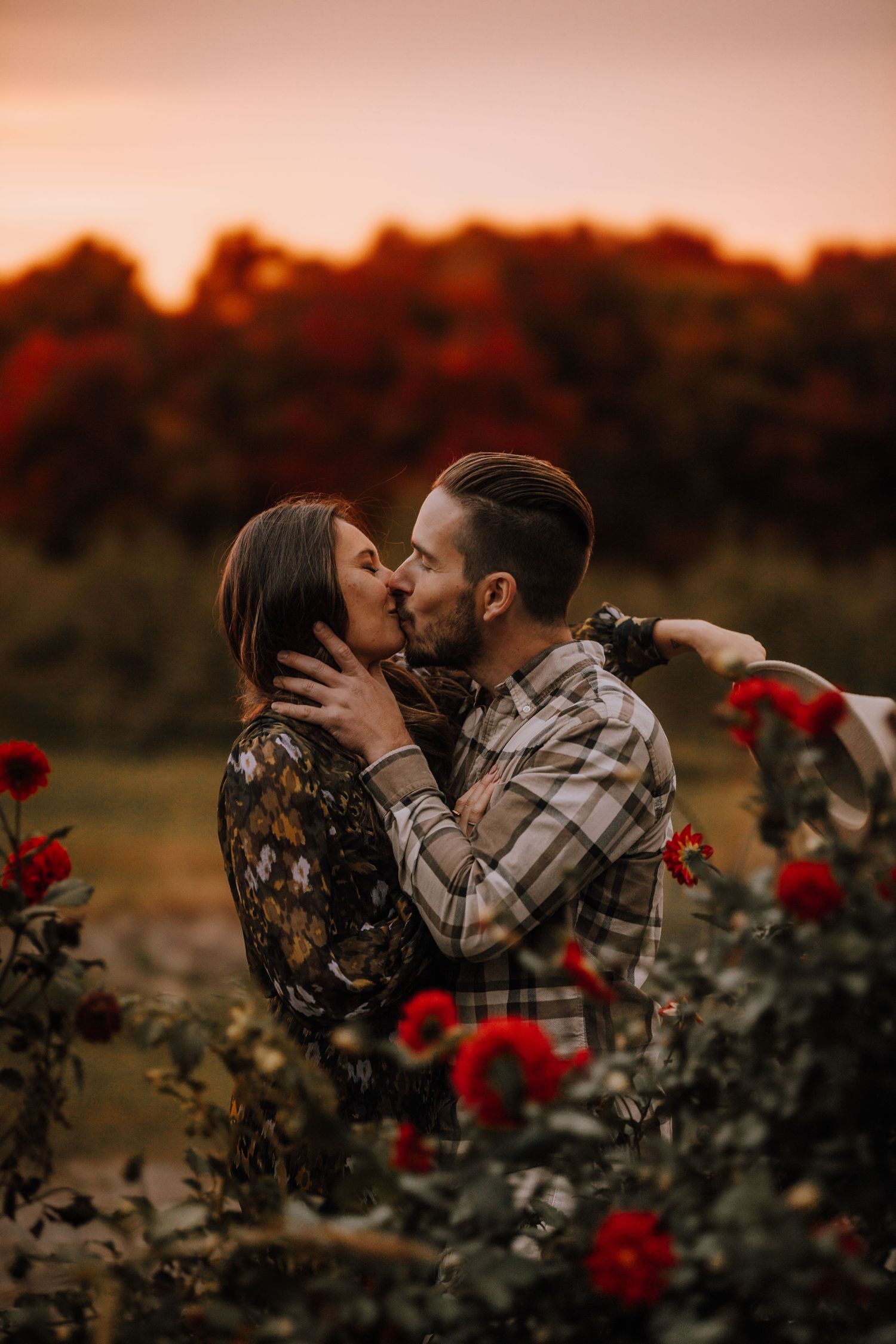 An intimate embrace surrounded by red roses at sunset in a garden.