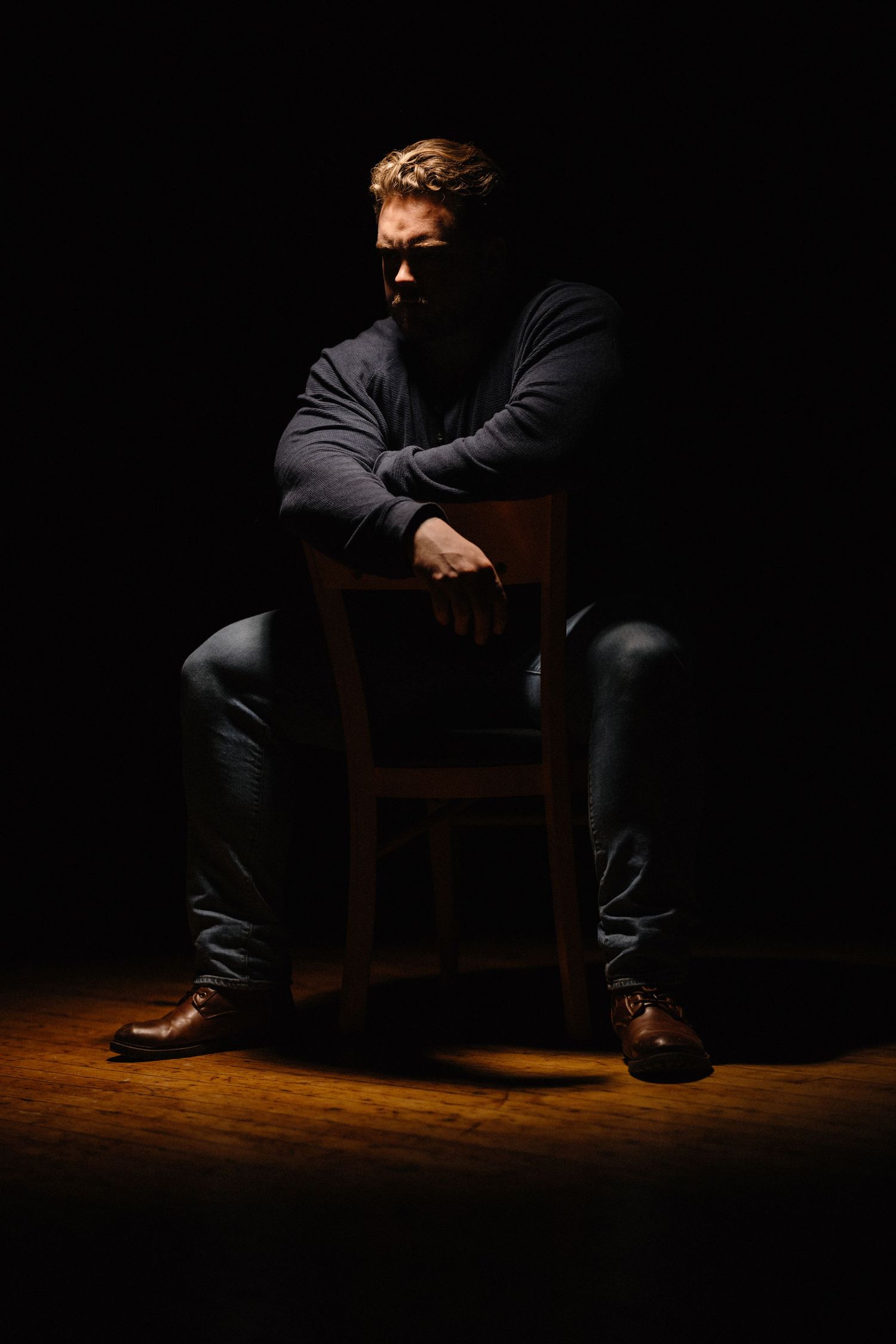 Dramatic low-key portrait series showing a person seated in shadows on wooden flooring.