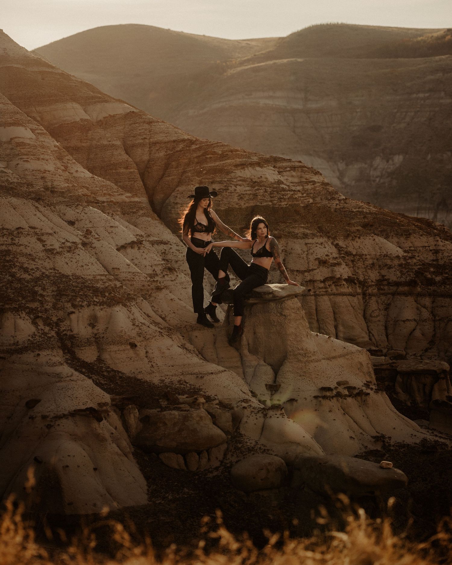 Two people posing dramatically on rocky desert cliffs at sunset.