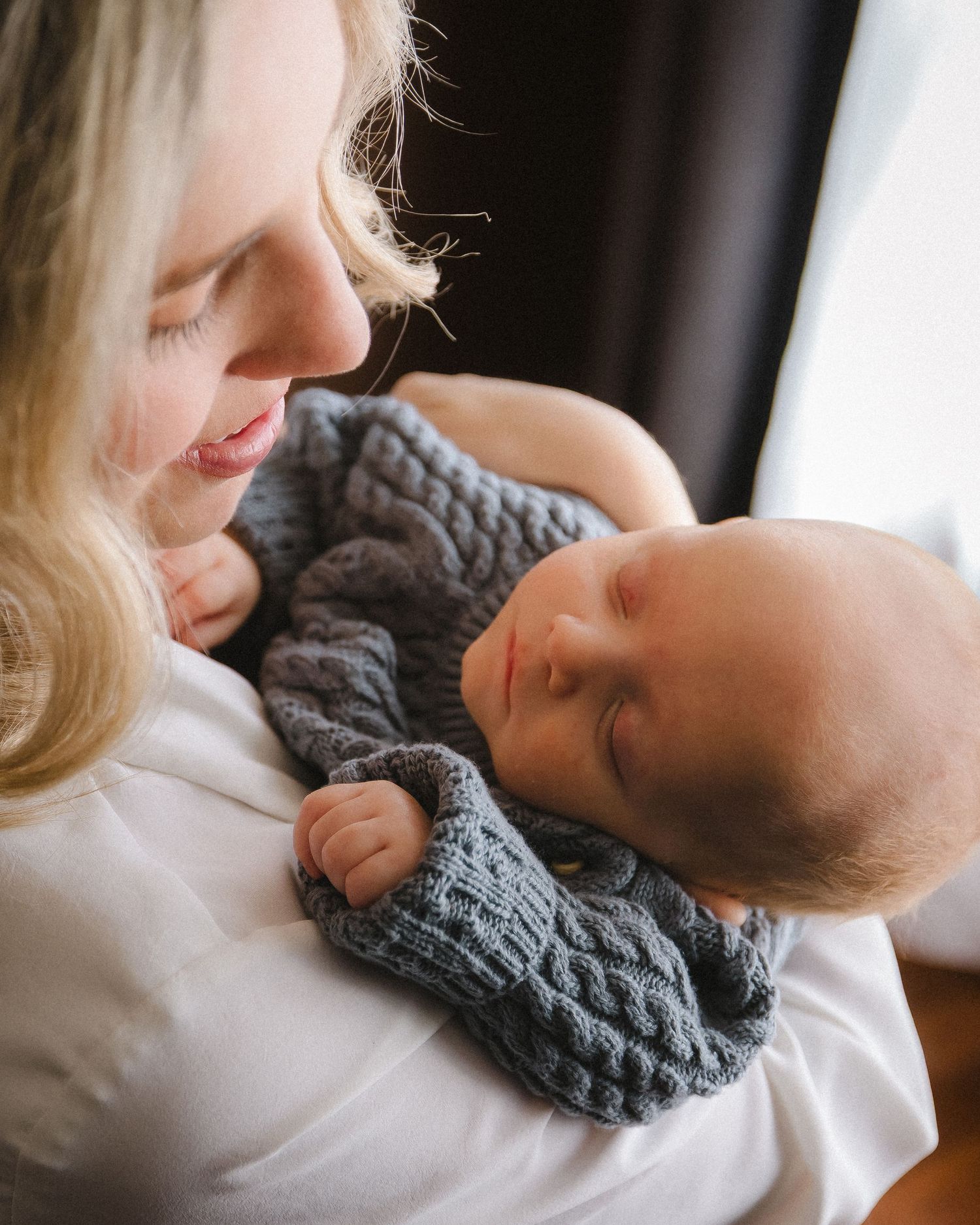 Intimate moment of parent holding sleeping baby in gray knit sweater.