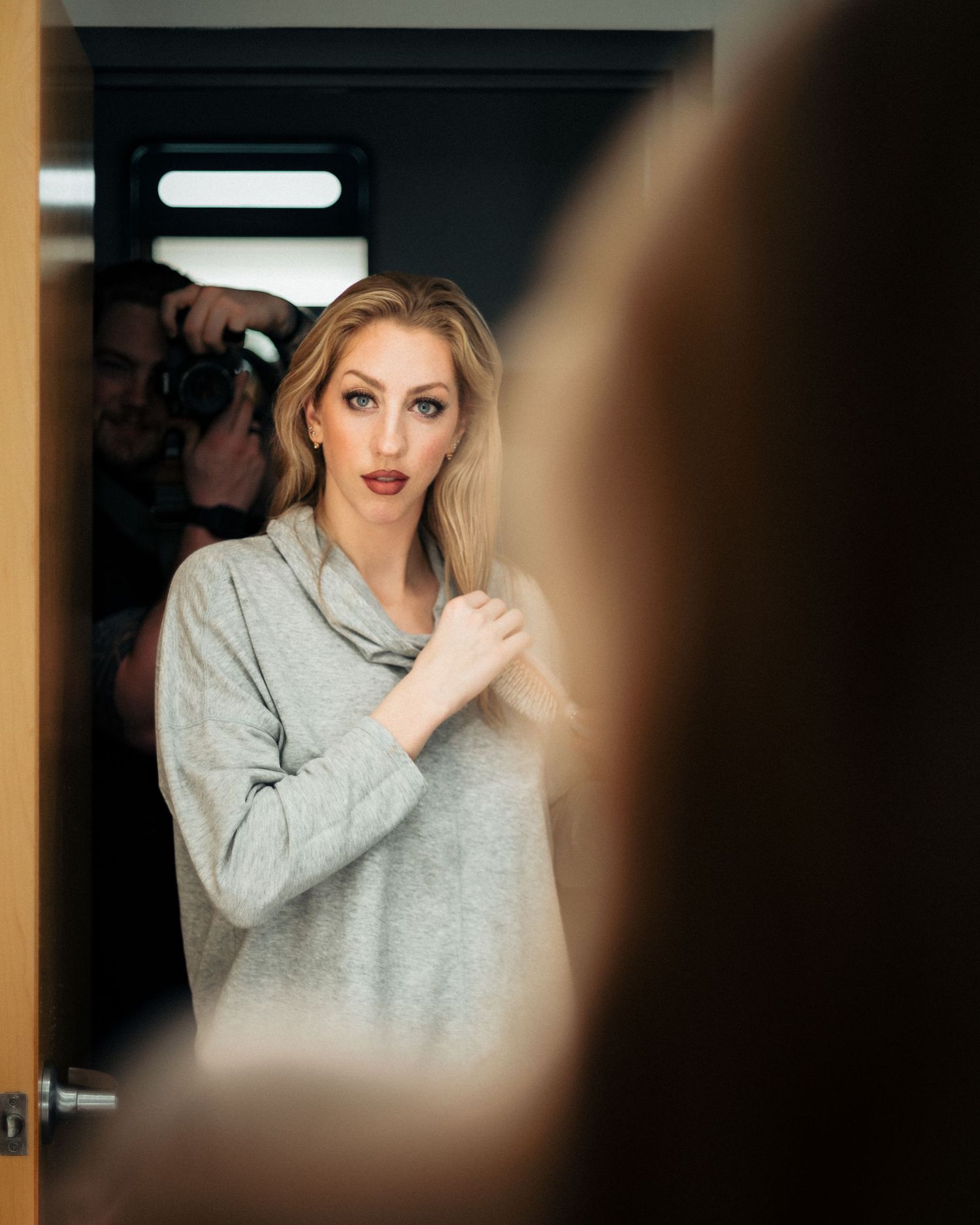 Woman in gray sweater looking at reflection in moody lighting.