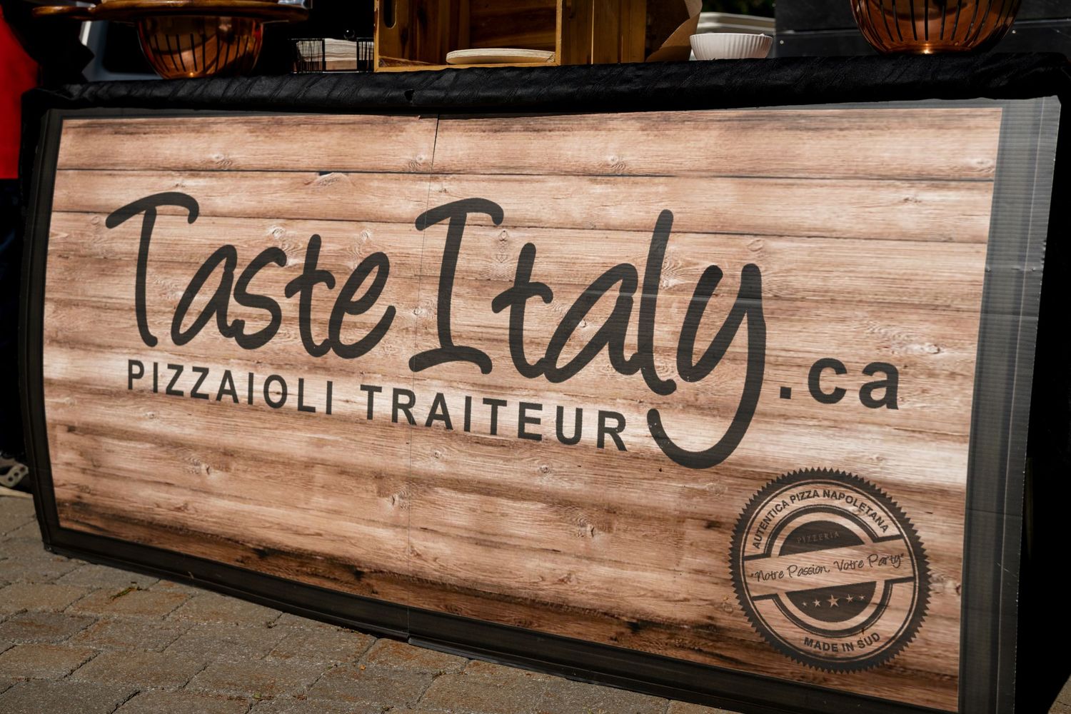 Wooden restaurant sign reading 'Taste Italy Pizzaioli Traiteur' mounted on wall.