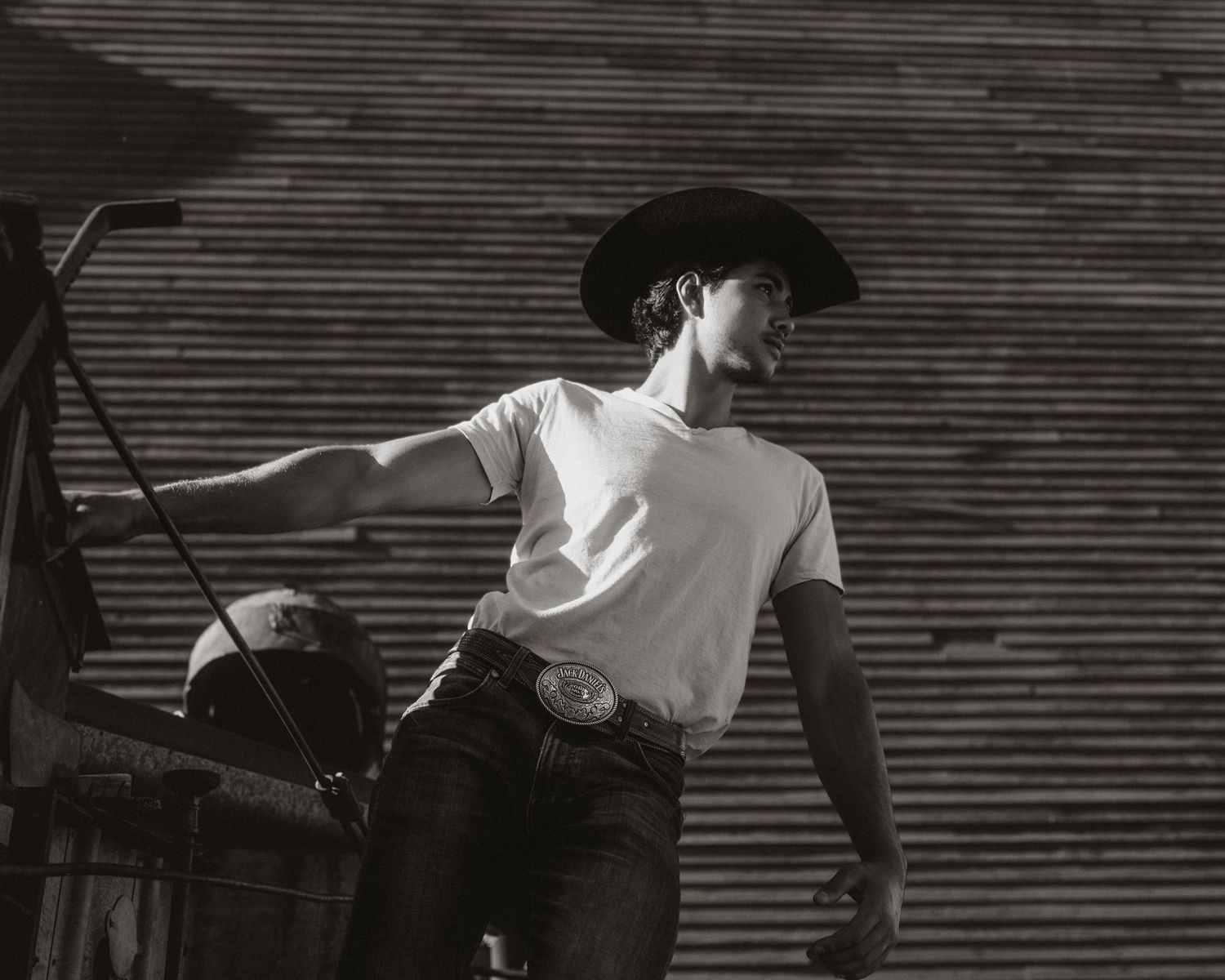 Black and white photo of person in western wear against industrial backdrop.