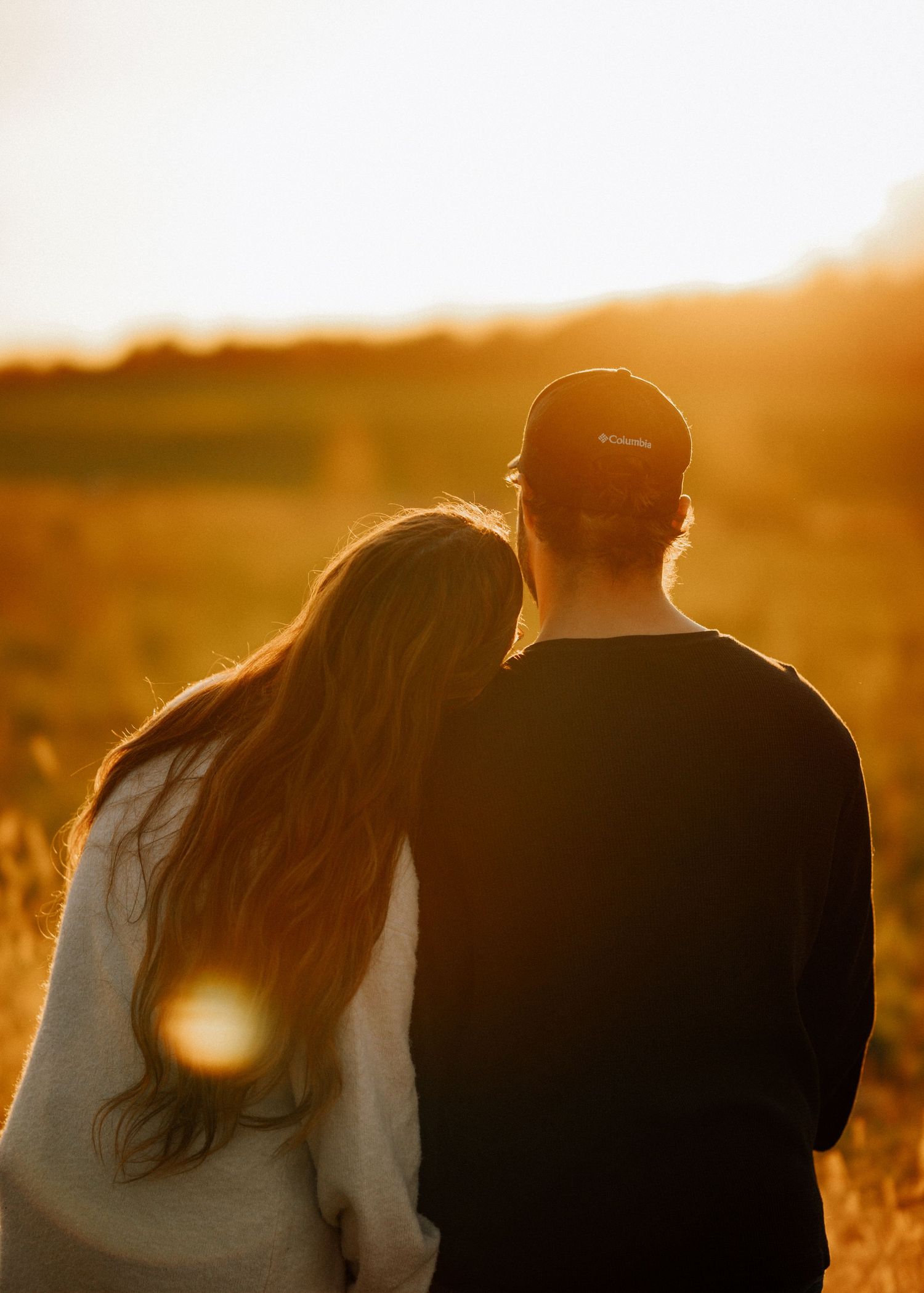 Backlit silhouettes of a couple standing close together in a golden field at sunset.