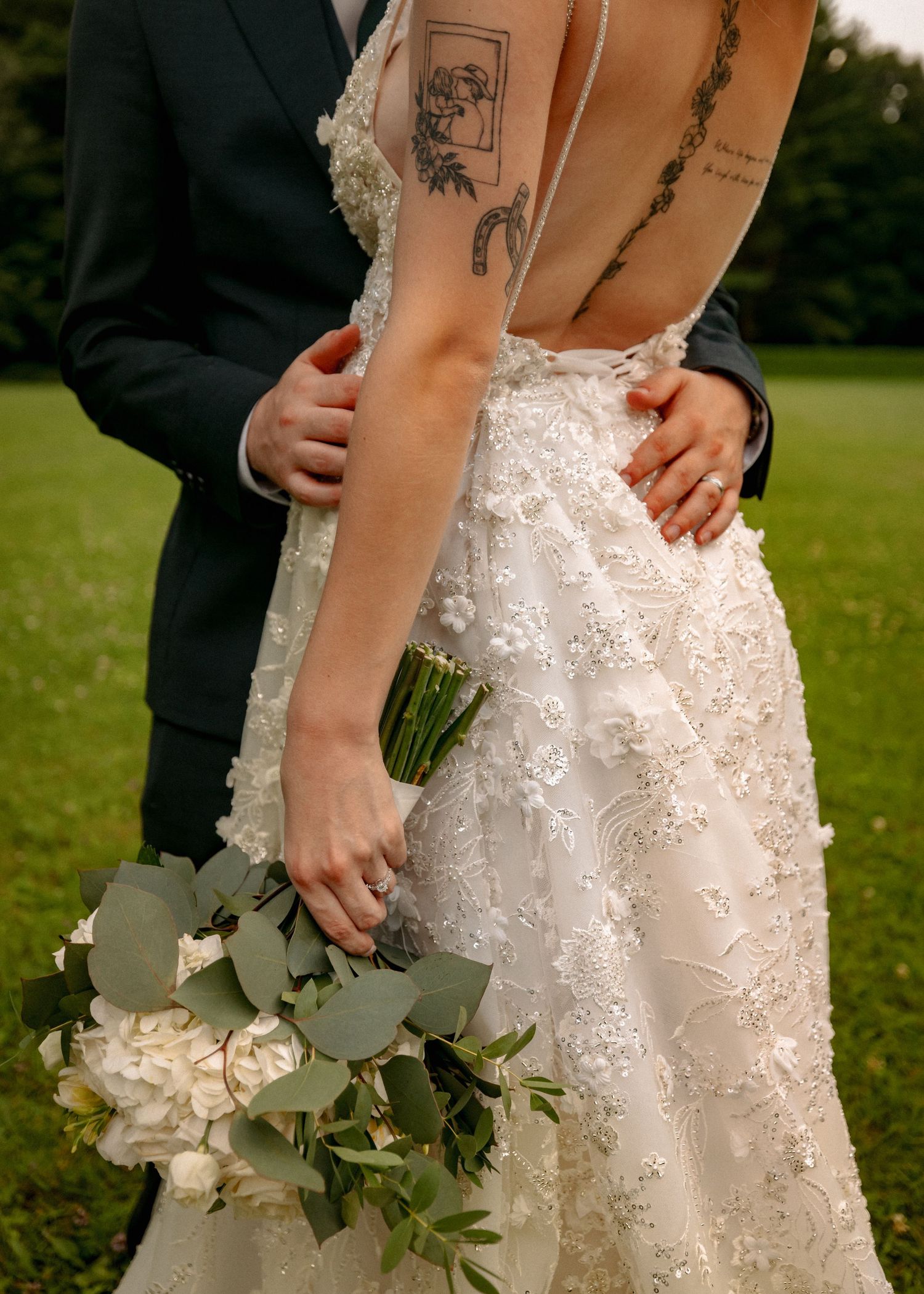 Close-up details of a lace wedding dress and bouquet with white flowers and greenery.