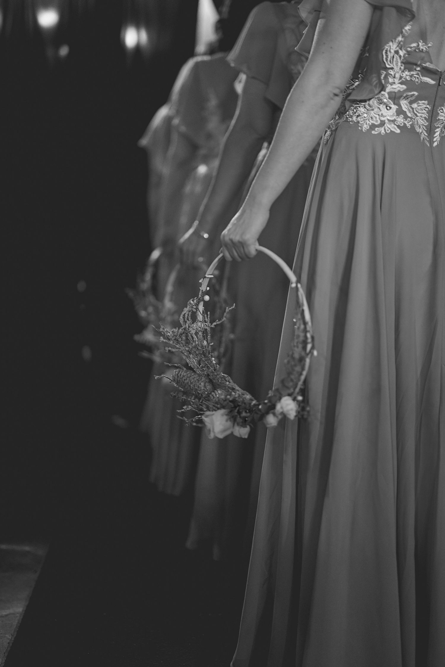 Bridesmaids in flowing dresses hold bouquets during evening wedding ceremony.