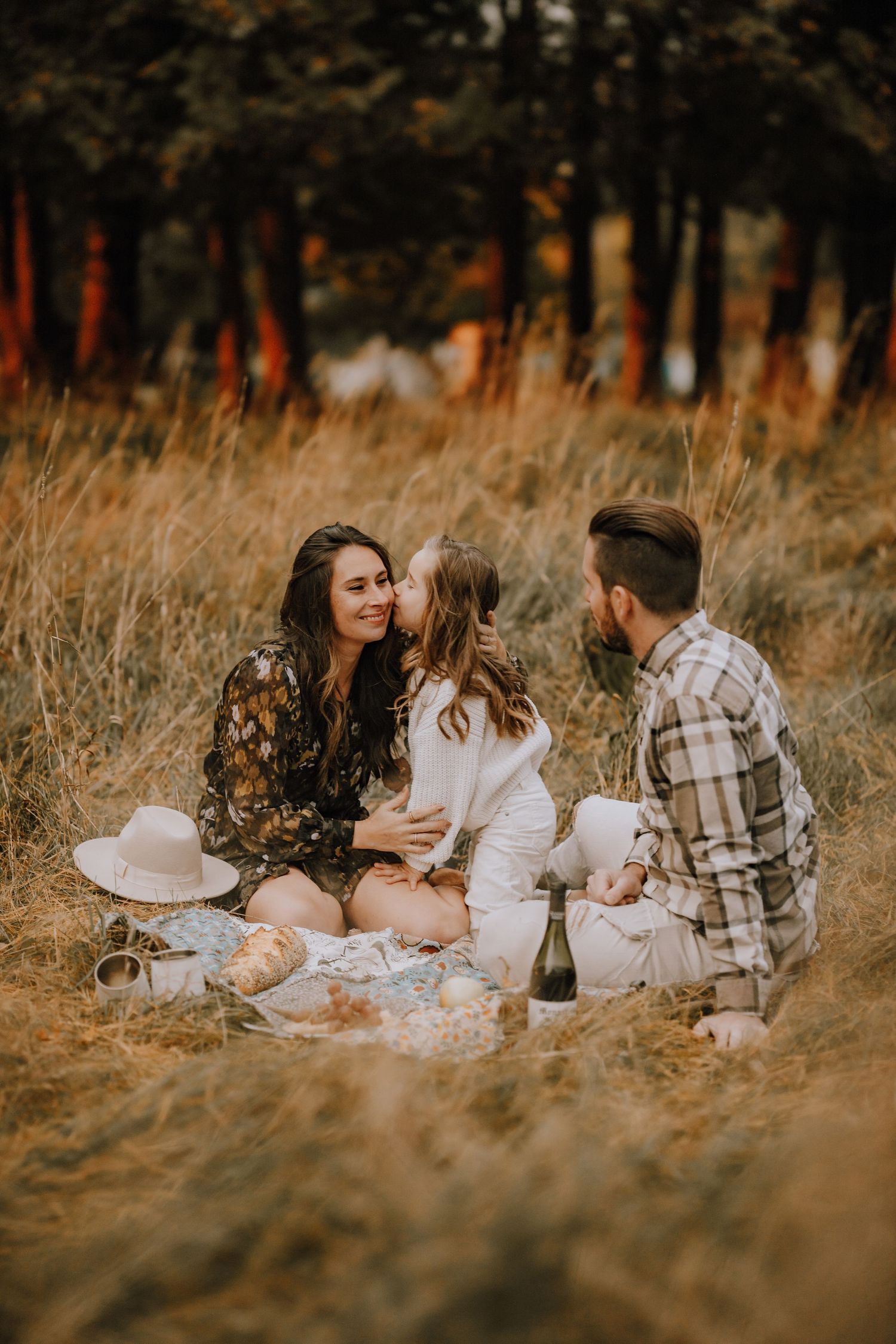A cozy autumn picnic scene with blankets and snacks laid out in golden grass at sunset.