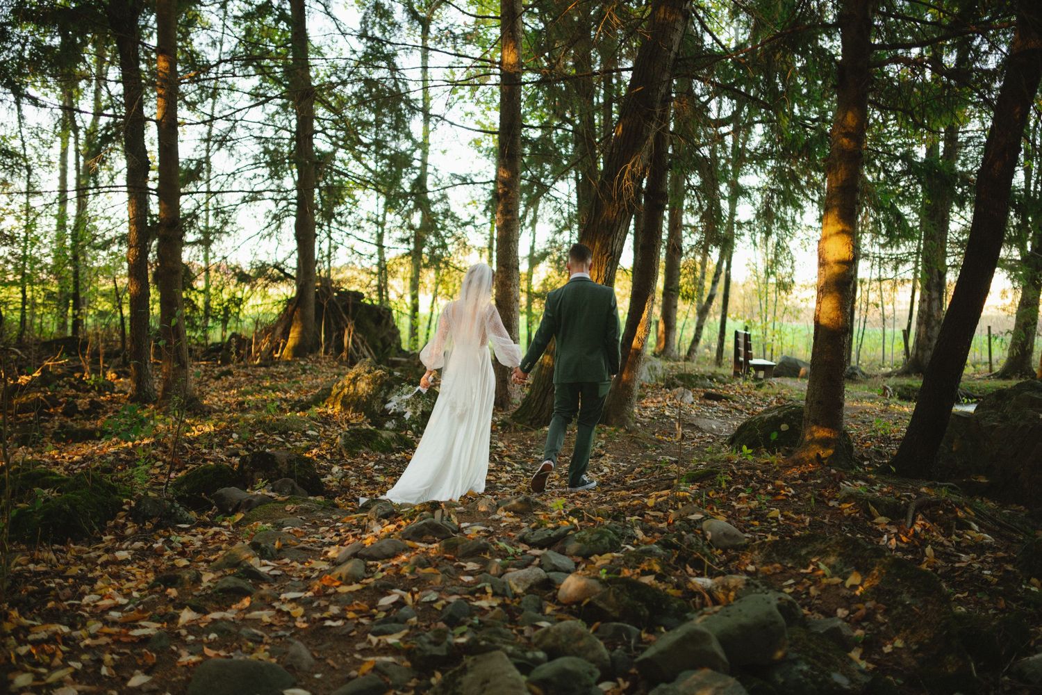 Newlyweds walking through a forest path during golden hour.