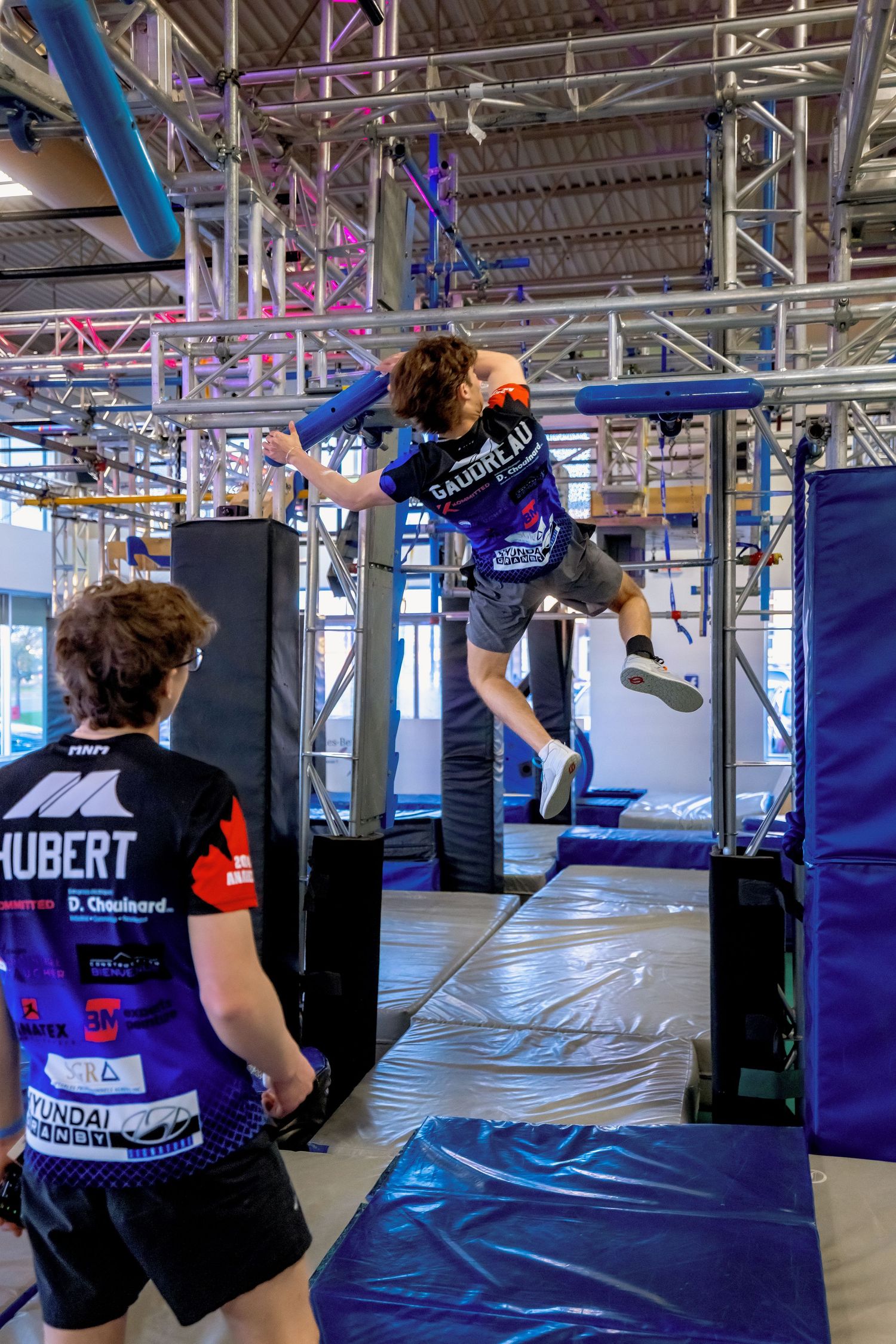 Athletes practicing parkour moves on suspended bars in an indoor training facility.