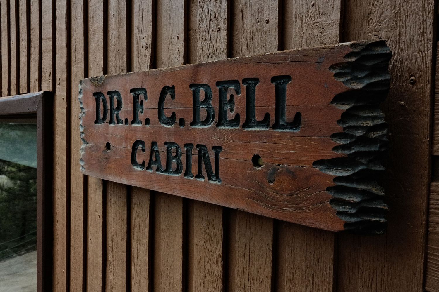 Rustic wooden sign reading Dr. F.C. Bell Cabin mounted on a wood-paneled wall in a natural outdoor setting.