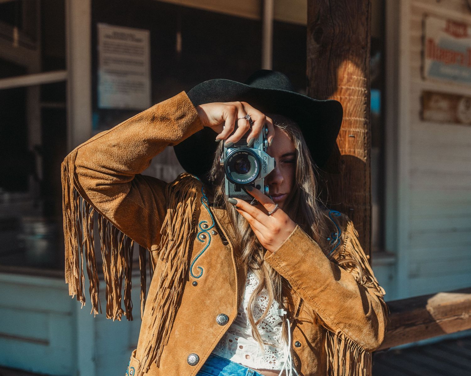 Western-style fashion shot featuring fringe jacket and dark hat.