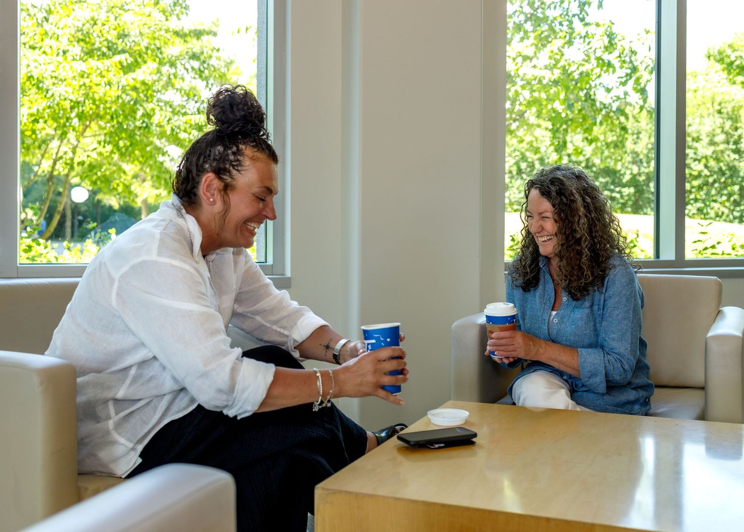 Casual meeting scene with people gathered around a white table near large windows.