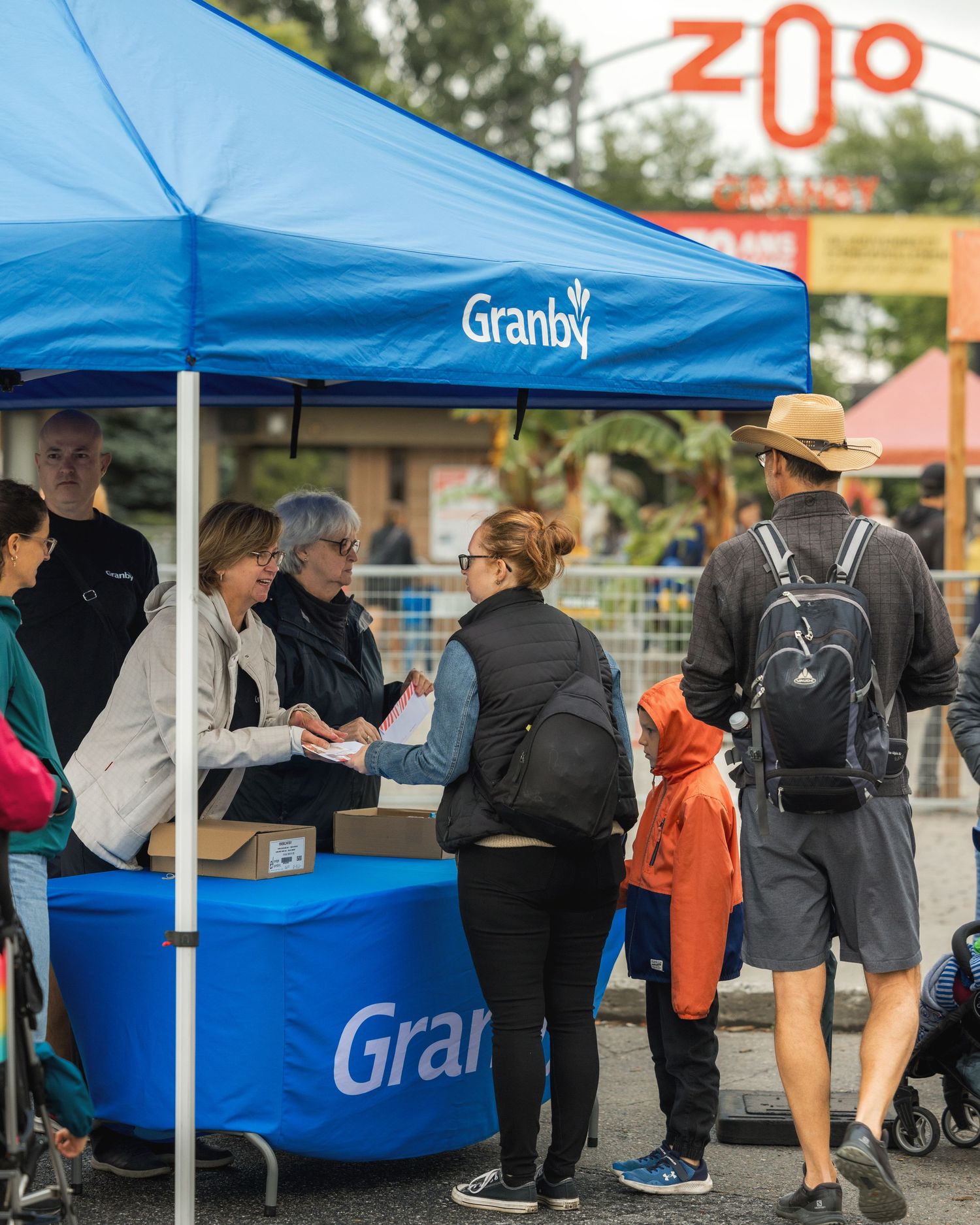 People gathering under blue canopy tents at an outdoor event.