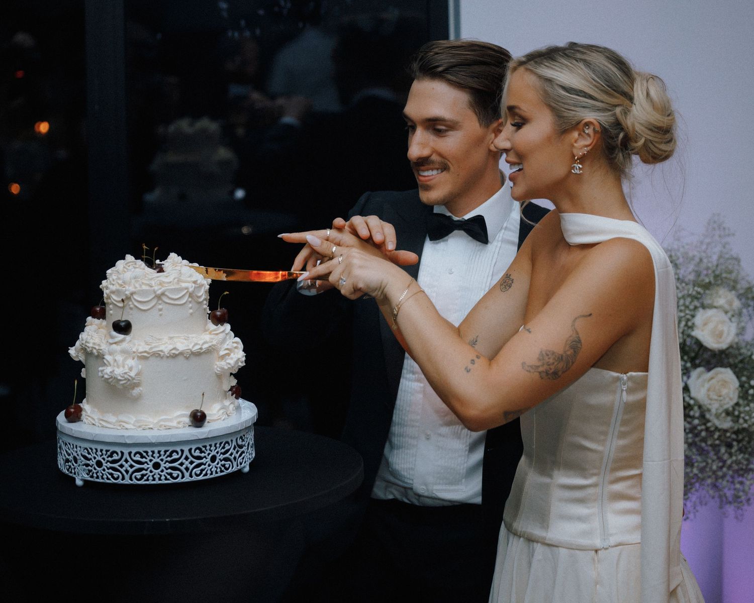 Elegant wedding cake cutting scene with ornate white tiers and decorative black trim pattern.