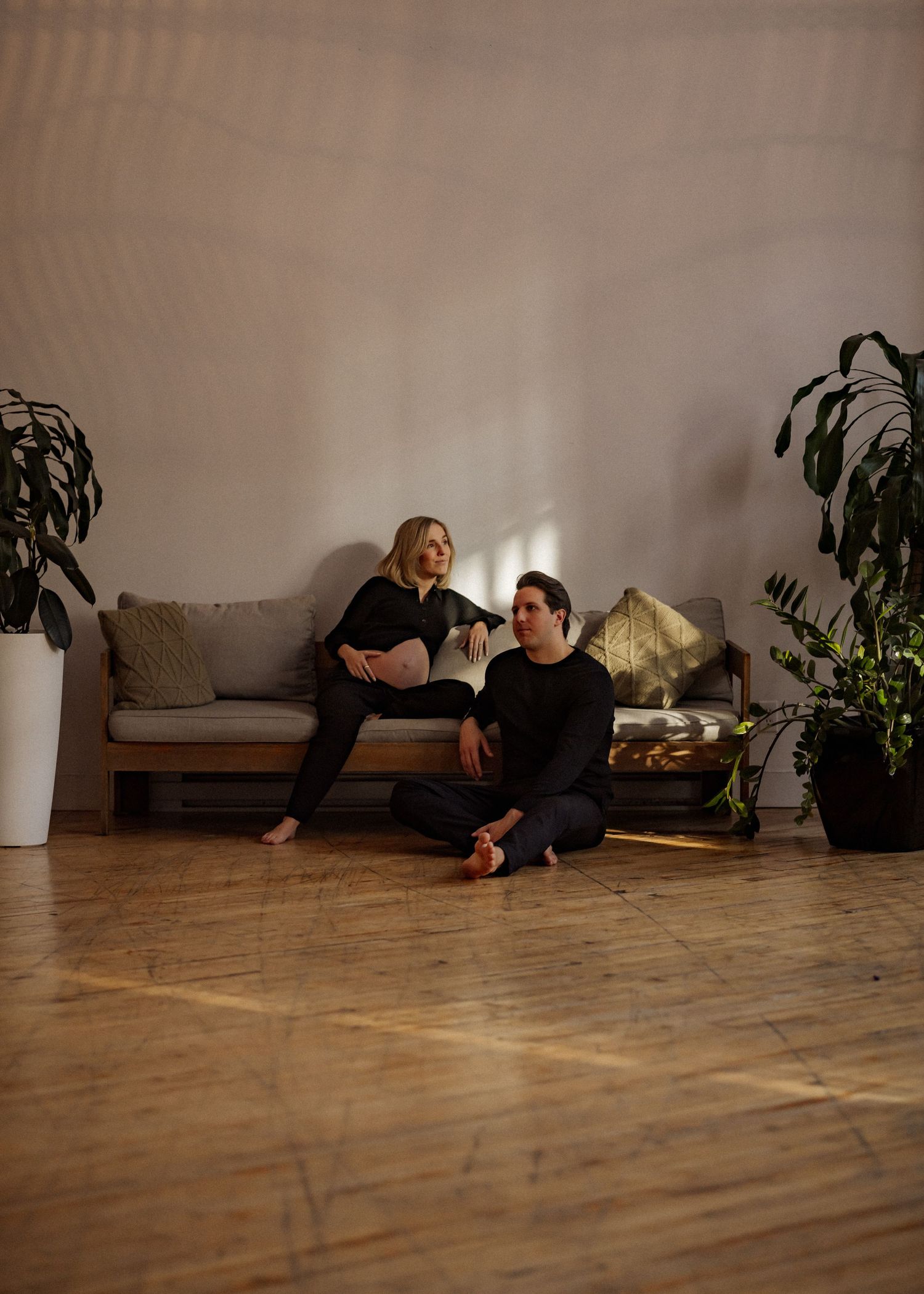 Couple relaxing on floor in minimalist living room with plants and soft lighting.