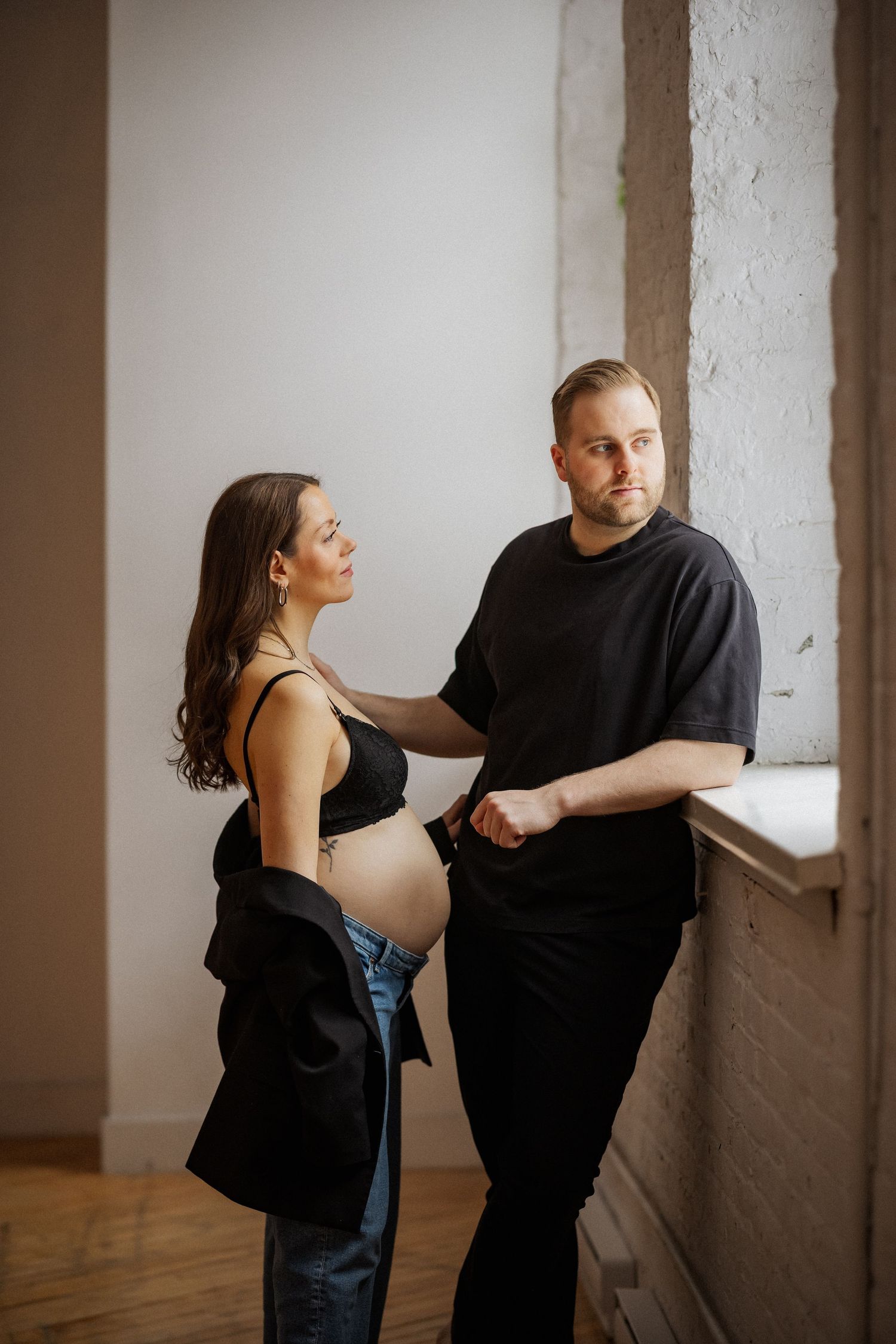 Couple in casual attire interacting near white wall in minimalist setting.