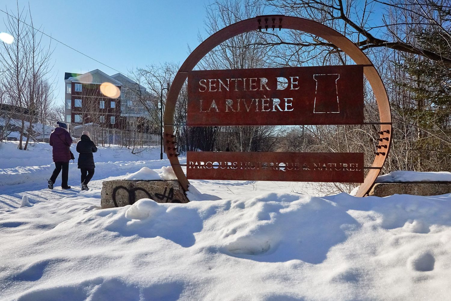 Snow-covered winter landscape with wooden welcome sign and park entrance.