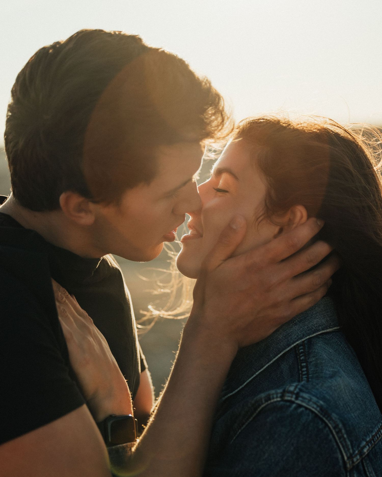 Backlit couple sharing passionate moment during golden hour.