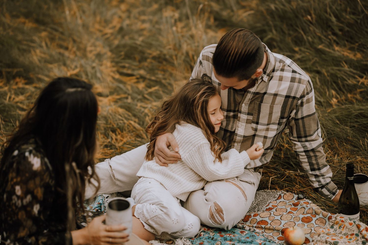 A tender family moment during an autumn picnic in a field of tall grass.