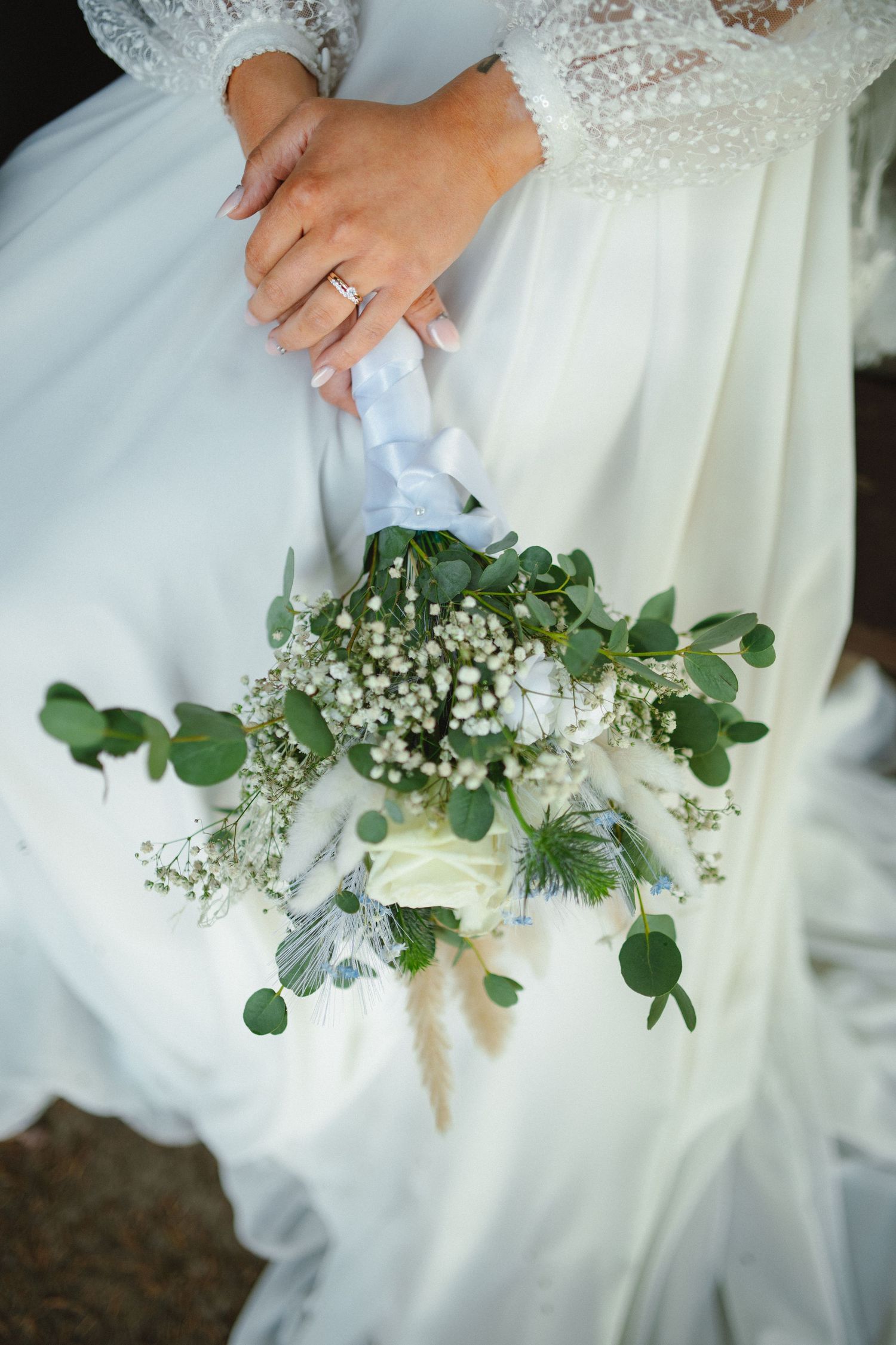 Wedding bouquet of white flowers and eucalyptus held against flowing white dress fabric.