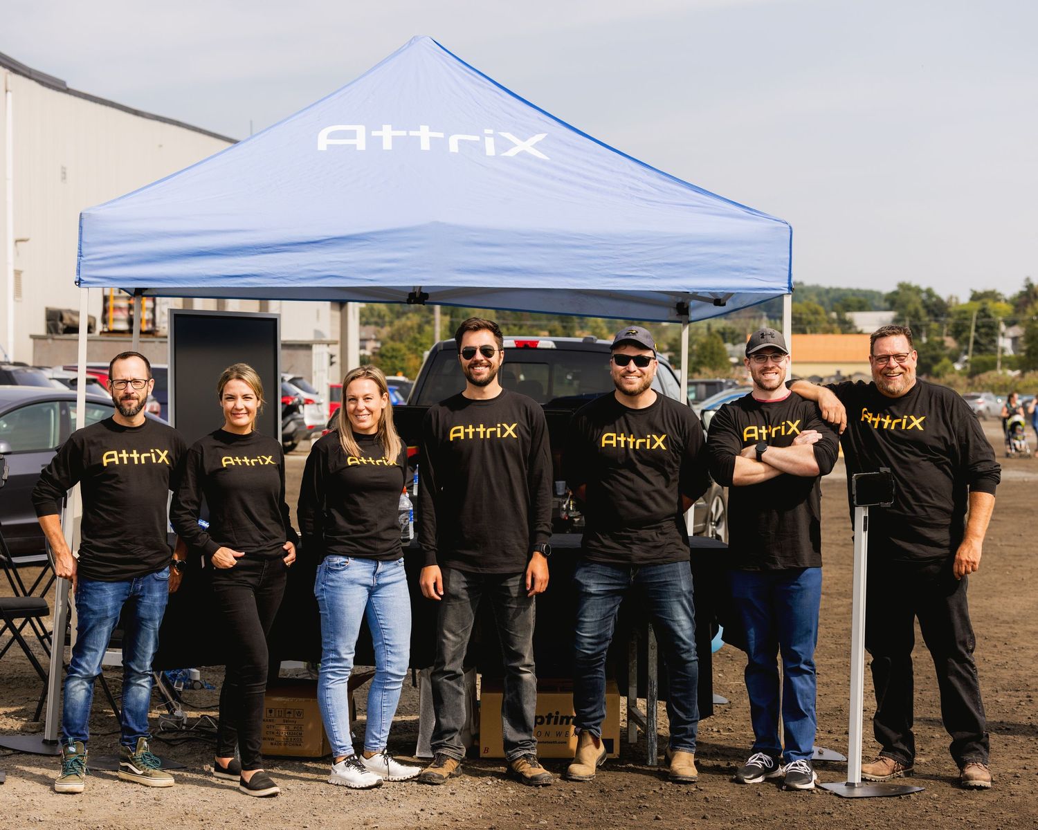 Large group of staff members lined up wearing matching black uniforms under a blue tent.
