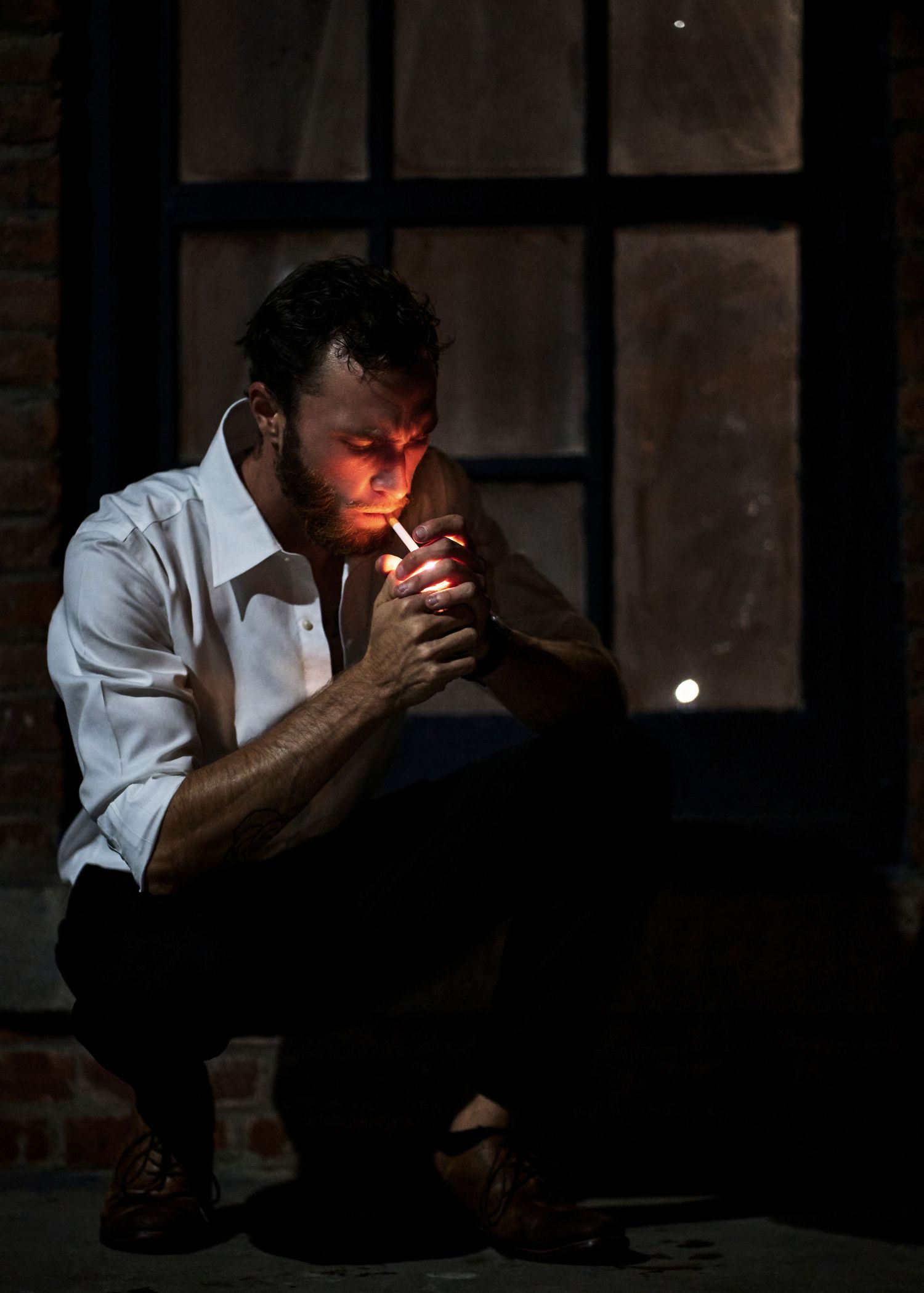 Person lighting cigarette in dramatic low-key lighting against dark background.