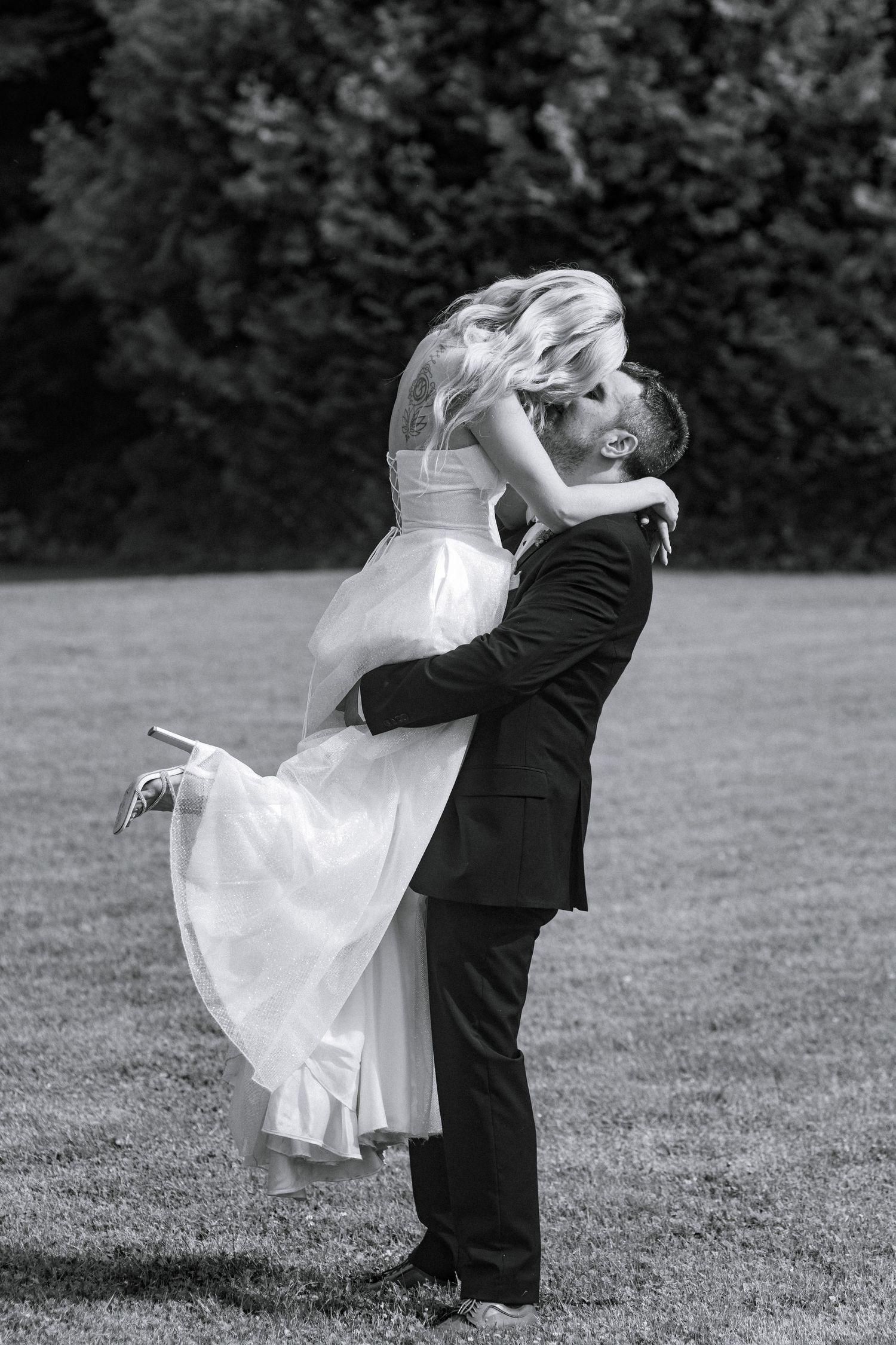 Black and white wedding portrait of couple dancing on grass.