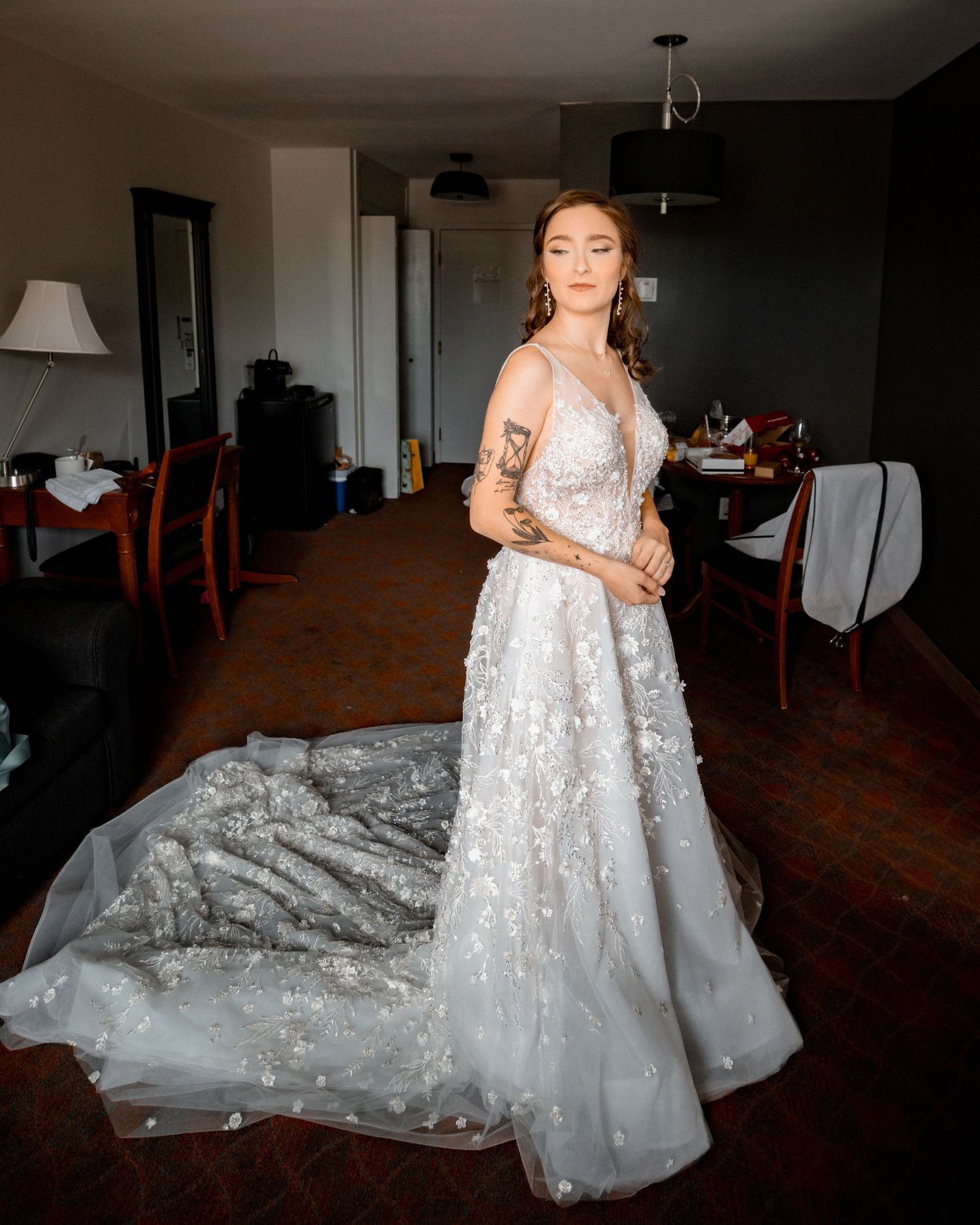 Elegant white lace wedding gown with flowing train in dimly lit room.