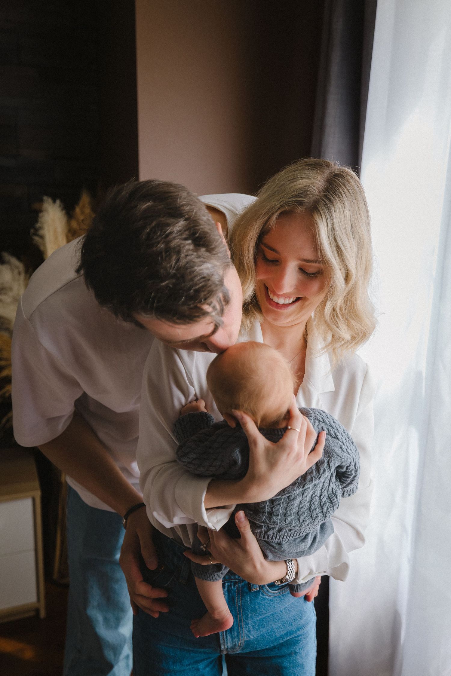 Family sharing an intimate moment with their newborn baby near a window.