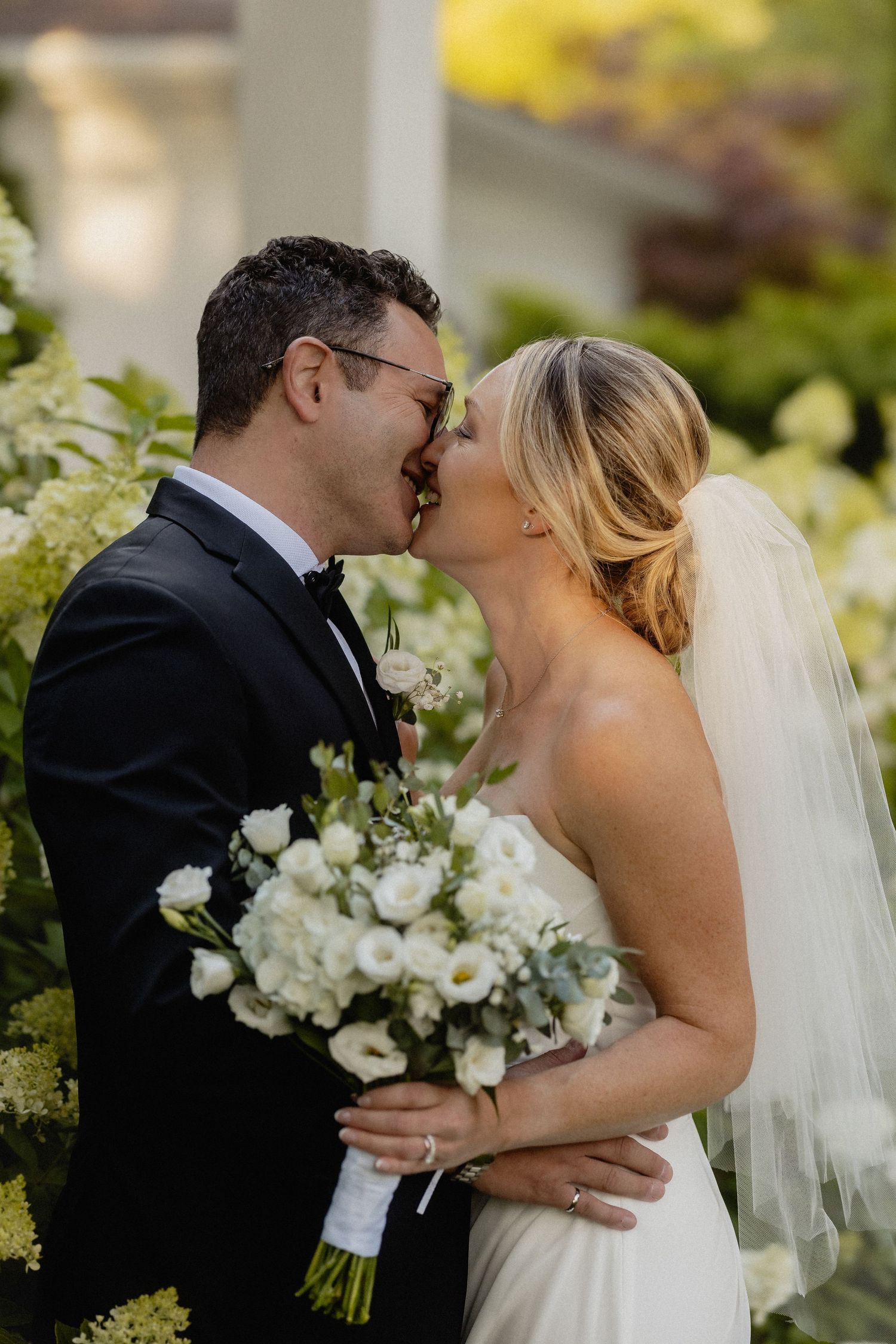 Romantic wedding portrait with white floral bouquet against garden backdrop.