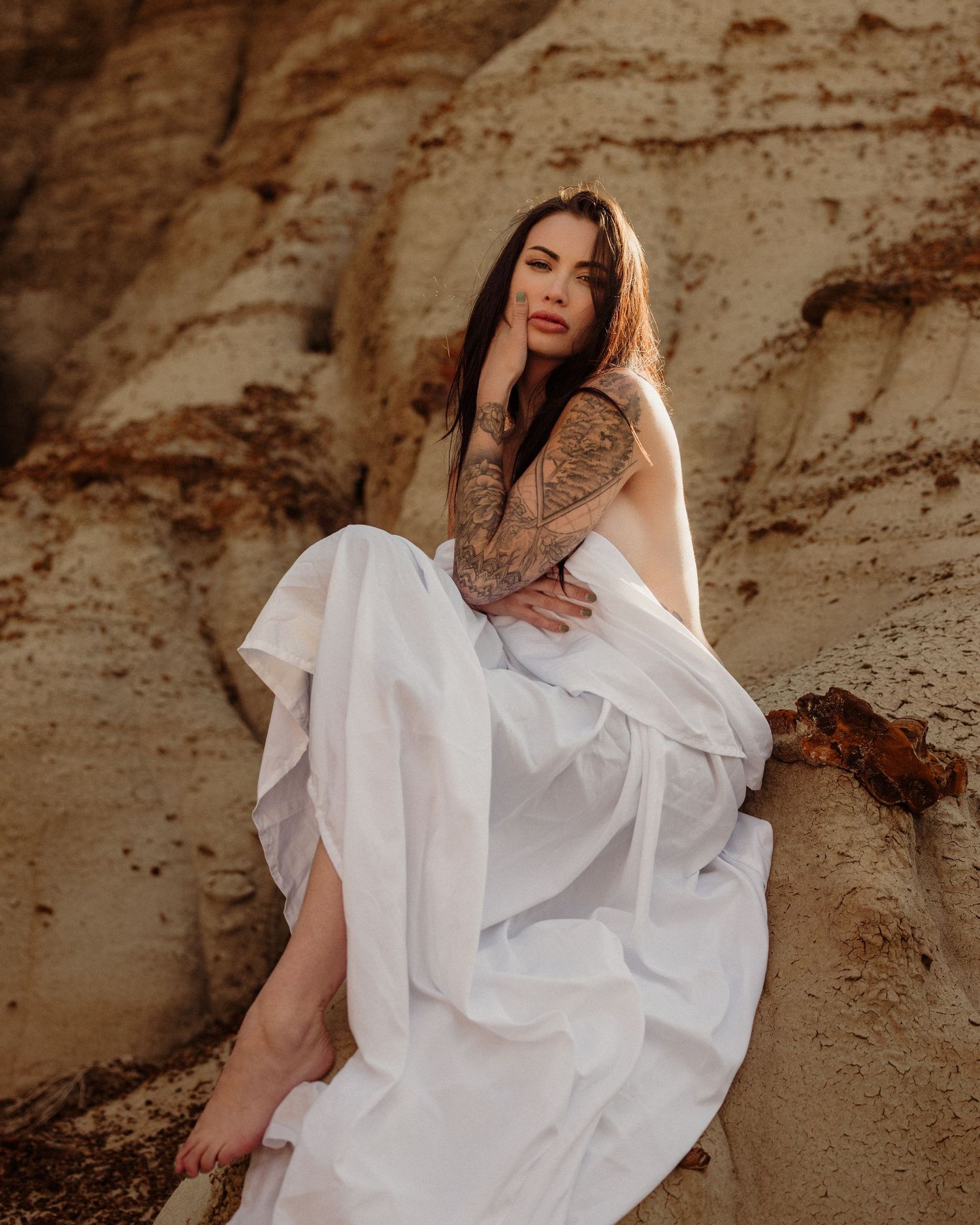 Person in flowing white dress poses against textured rock wall.