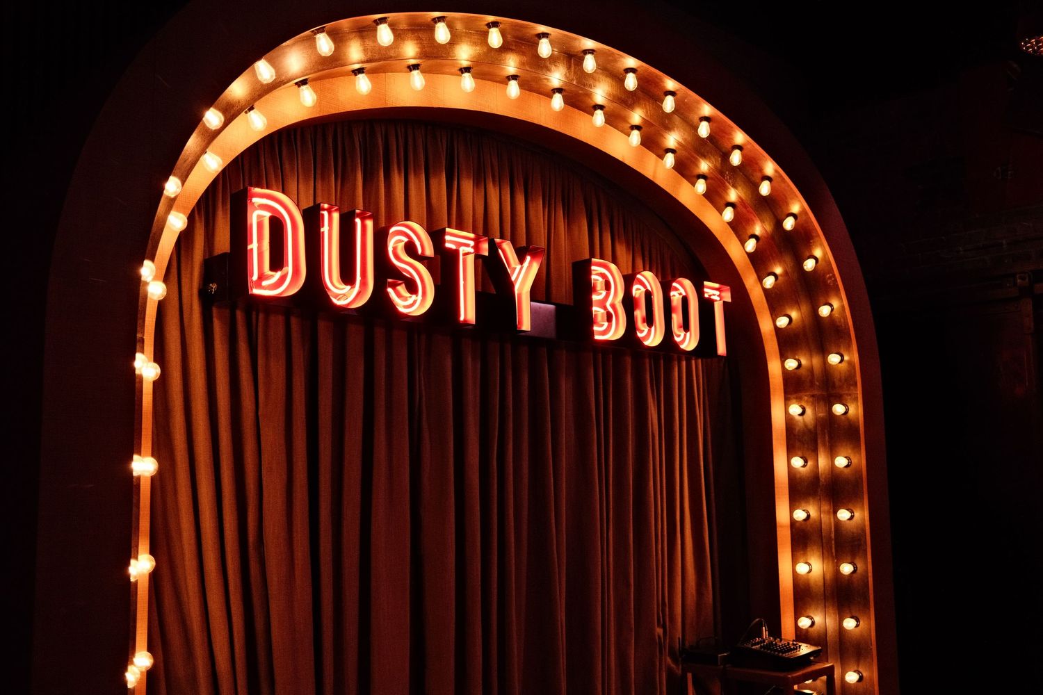 Dusty Boot venue entrance with marquee lights framing an arch over red curtain backdrop.