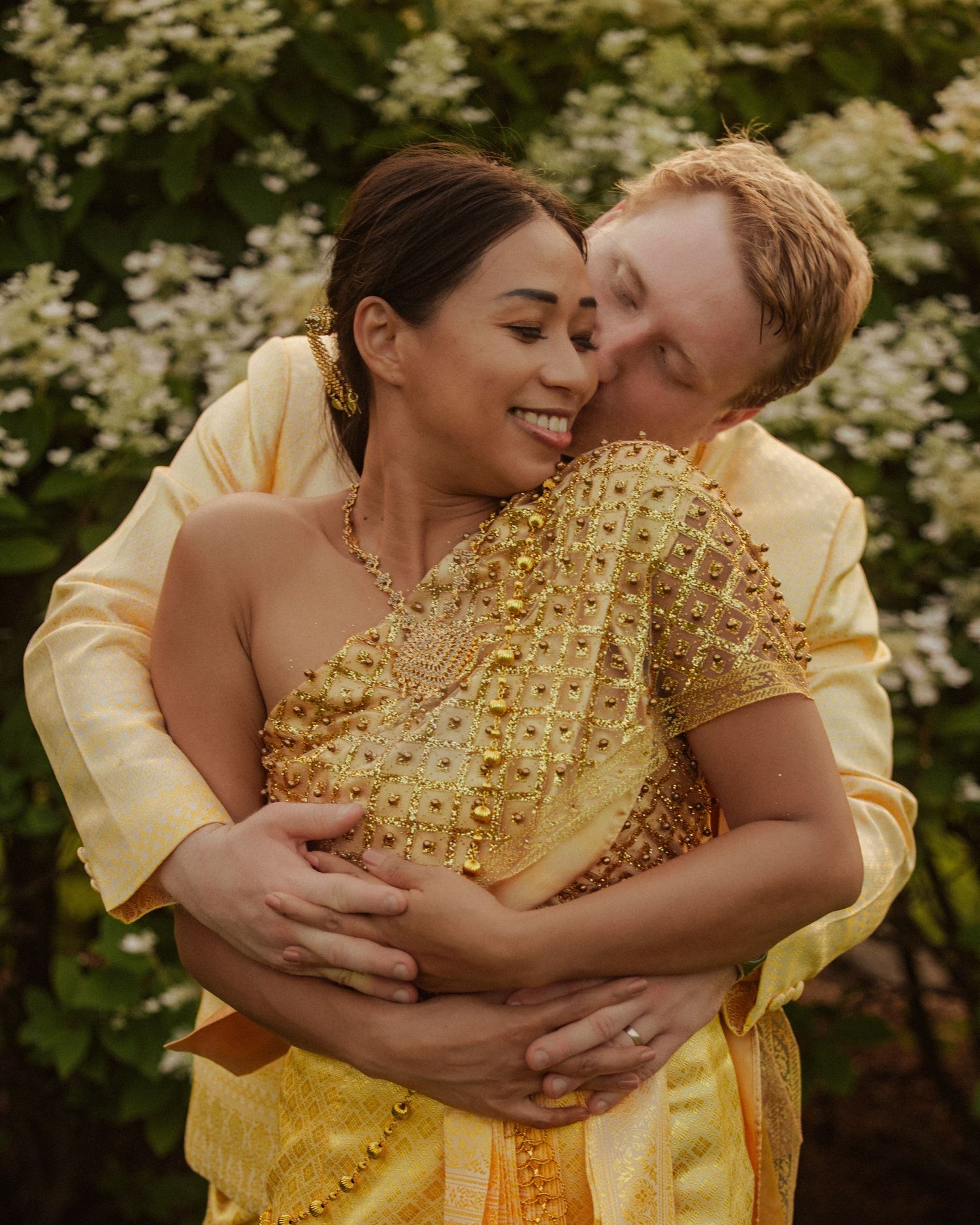 A tender moment captured between a couple wearing yellow formal attire surrounded by white blossoms.