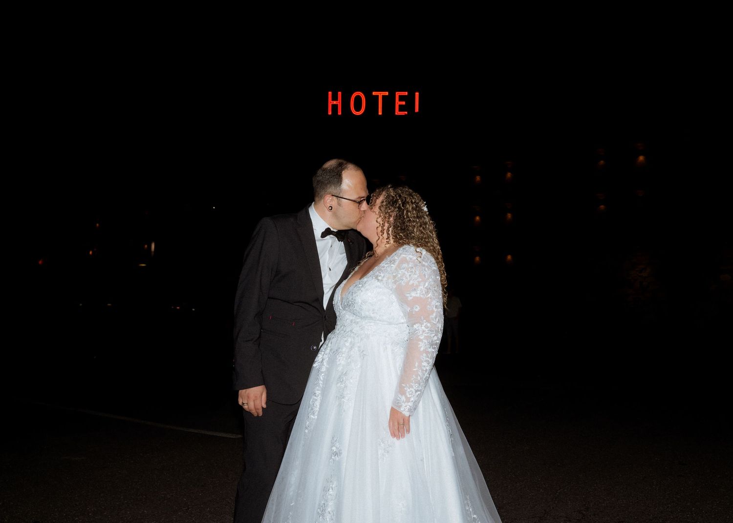 Silhouetted figures in formal attire dancing at a wedding reception with 'HOTEL' sign visible in background.