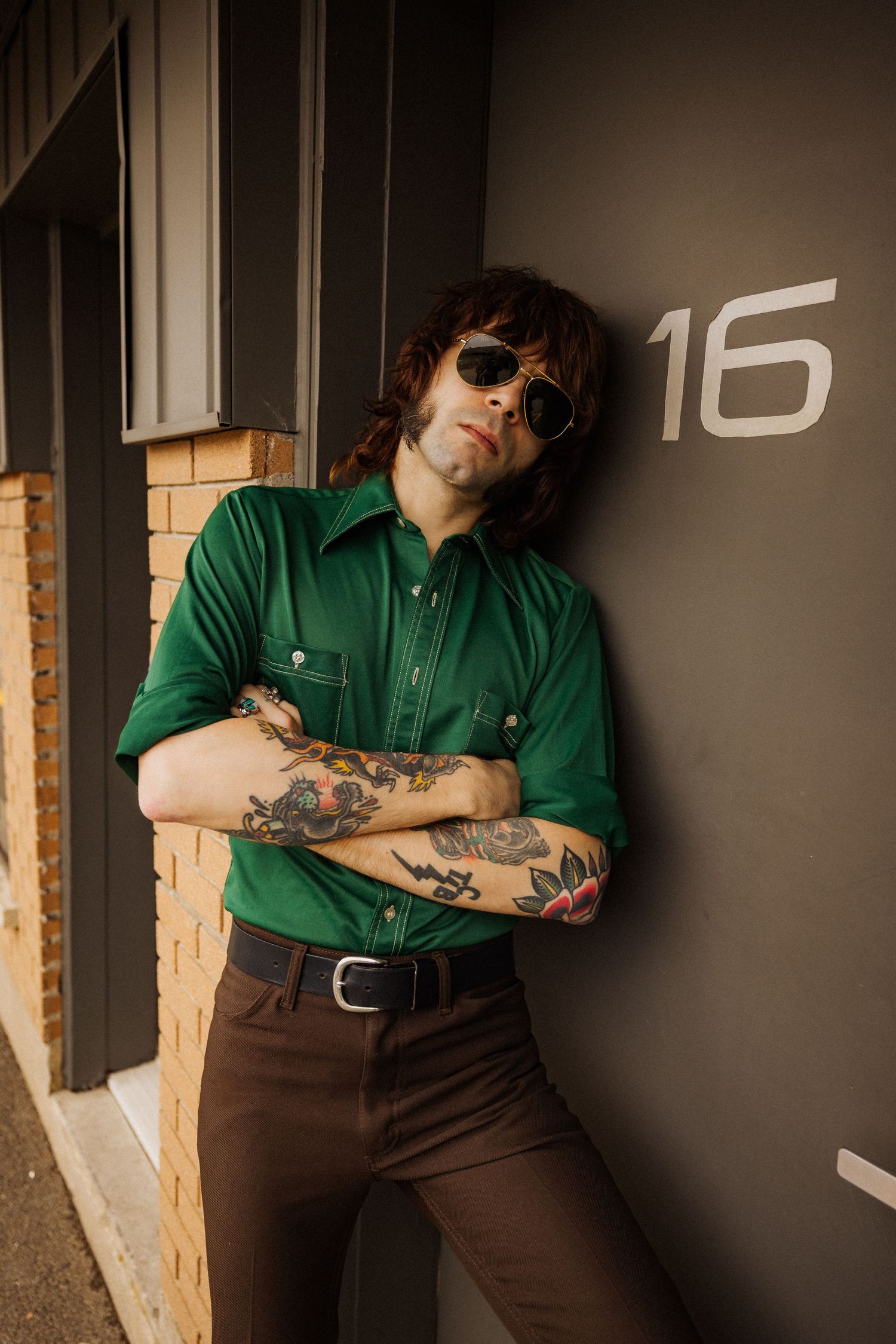 Casual portrait series against grey wall showing tattoos and green button-up shirt.