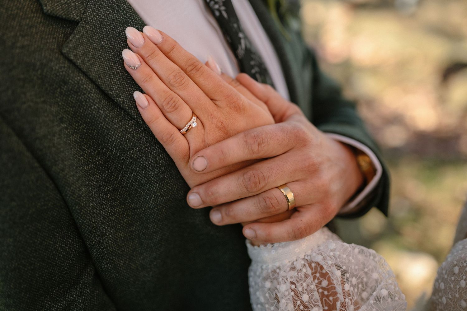 Close-up of intertwined hands with wedding rings against formal wedding attire.