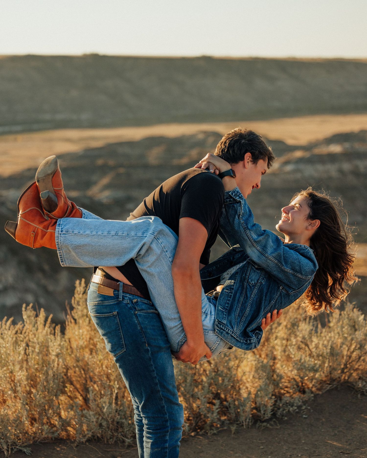 Playful couple in denim embracing outdoors during golden hour.