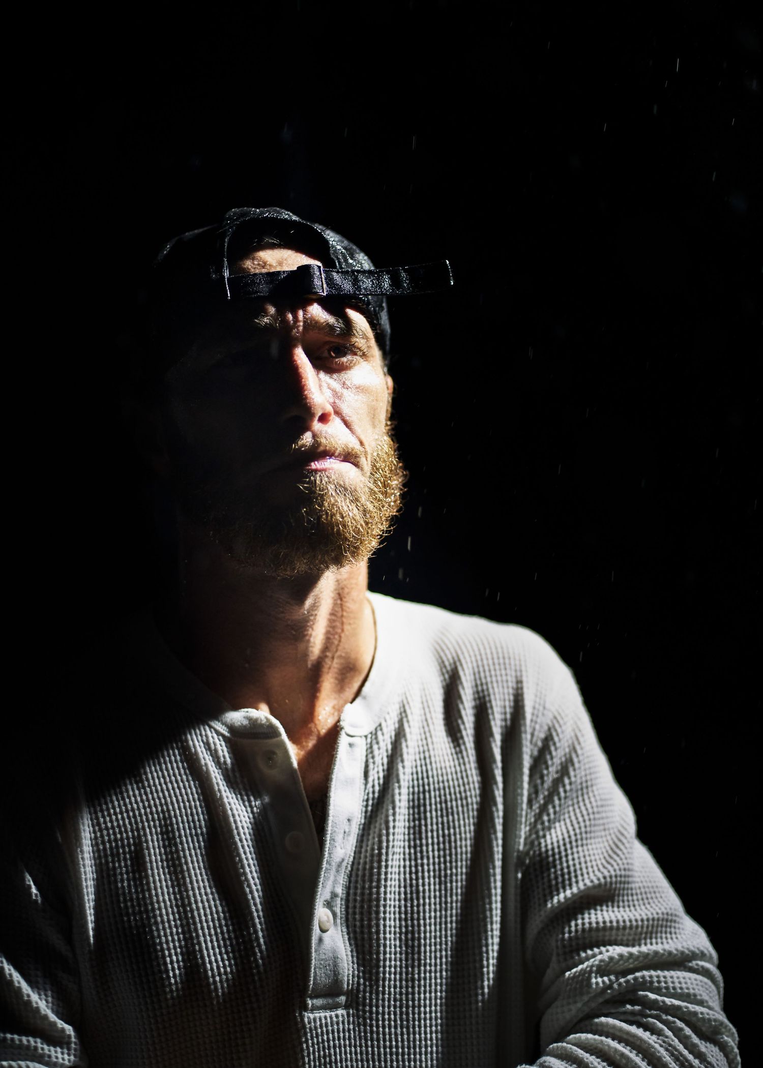 Moody low-key portrait showing dramatic side lighting on a person wearing a checkered shirt and cap.