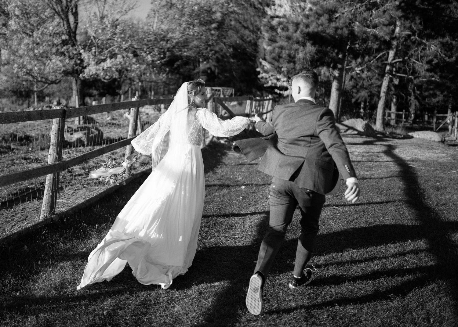 Black and white photo of newlyweds dancing playfully on grass.