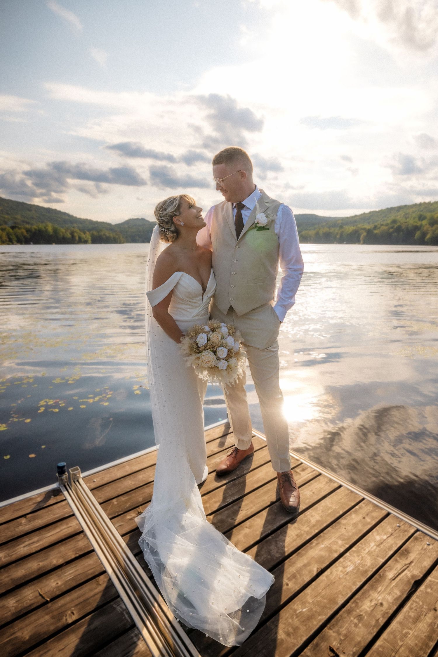 Romantic wedding photos on wooden dock with sunset over mountain lake.