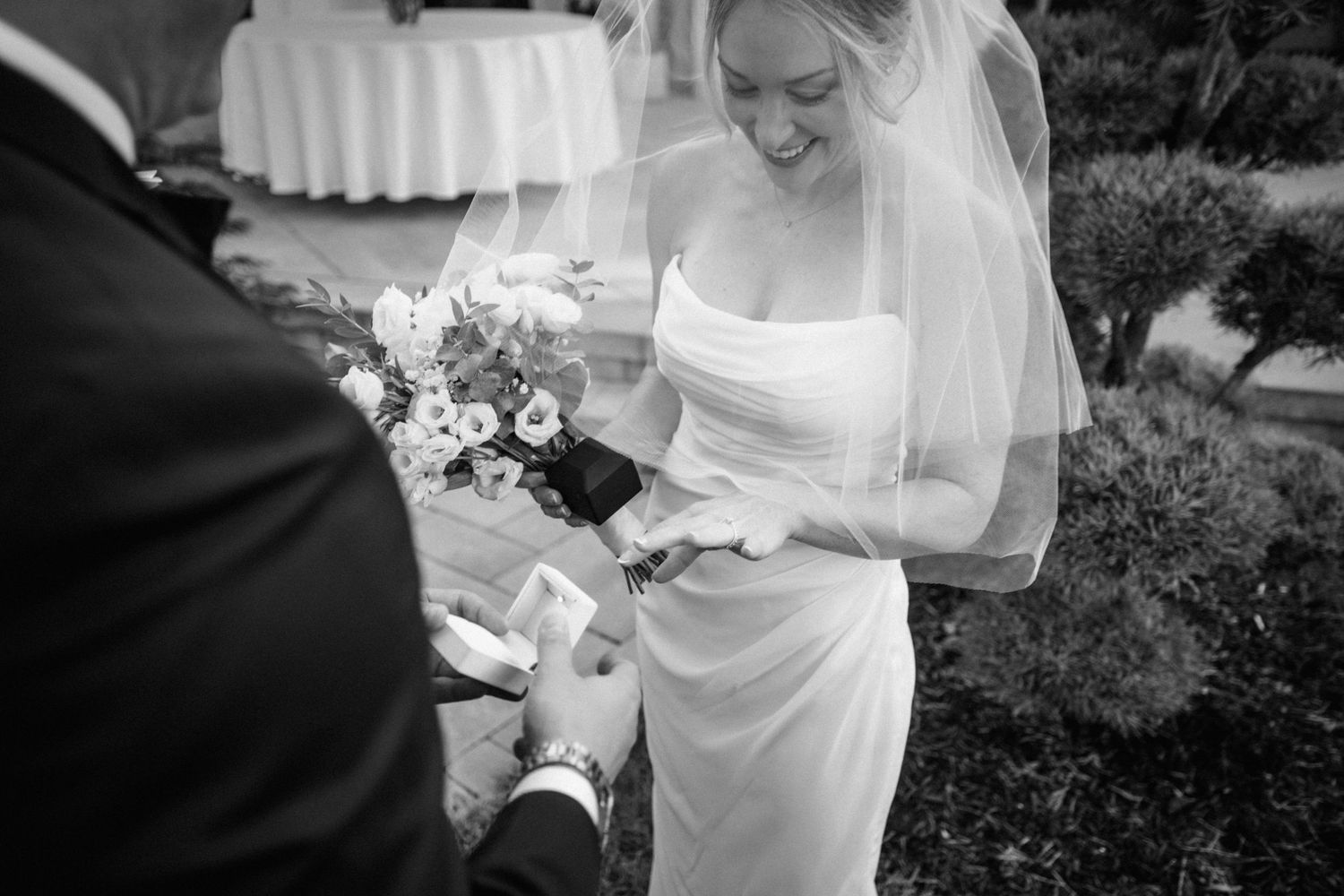 Black and white photo of a wedding ceremony showing exchange of rings with a bouquet of flowers.