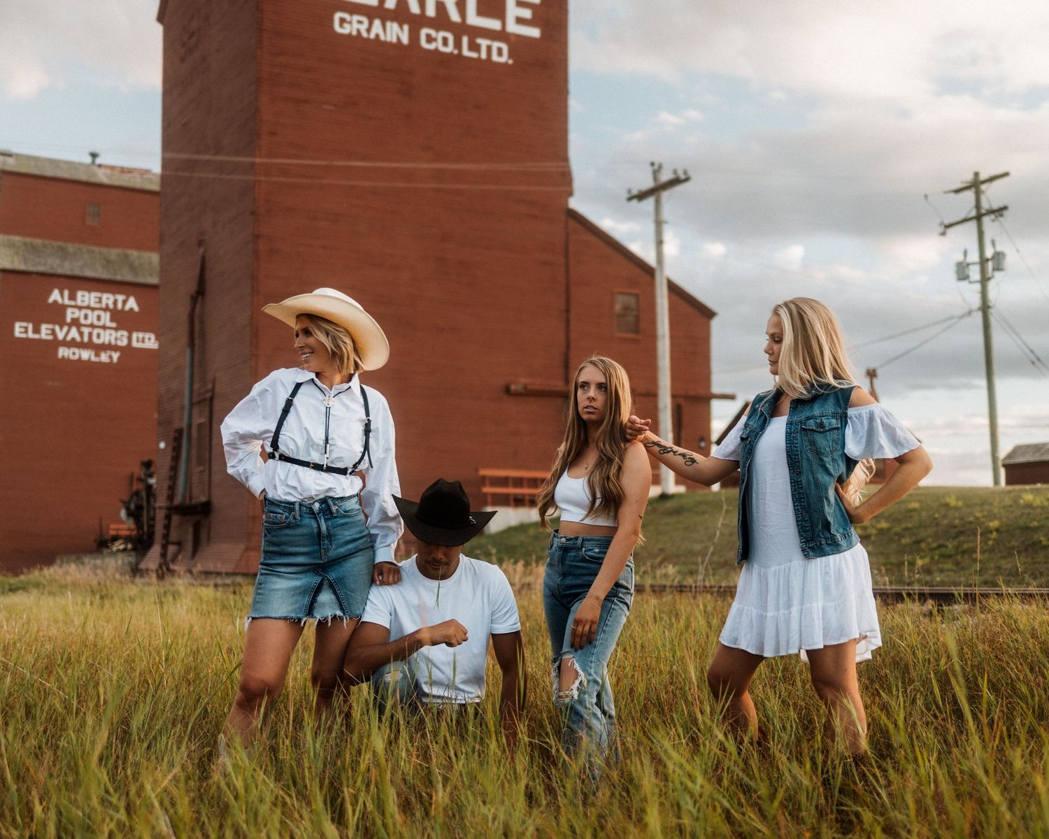 Group in western attire standing by brick building in grassland setting.