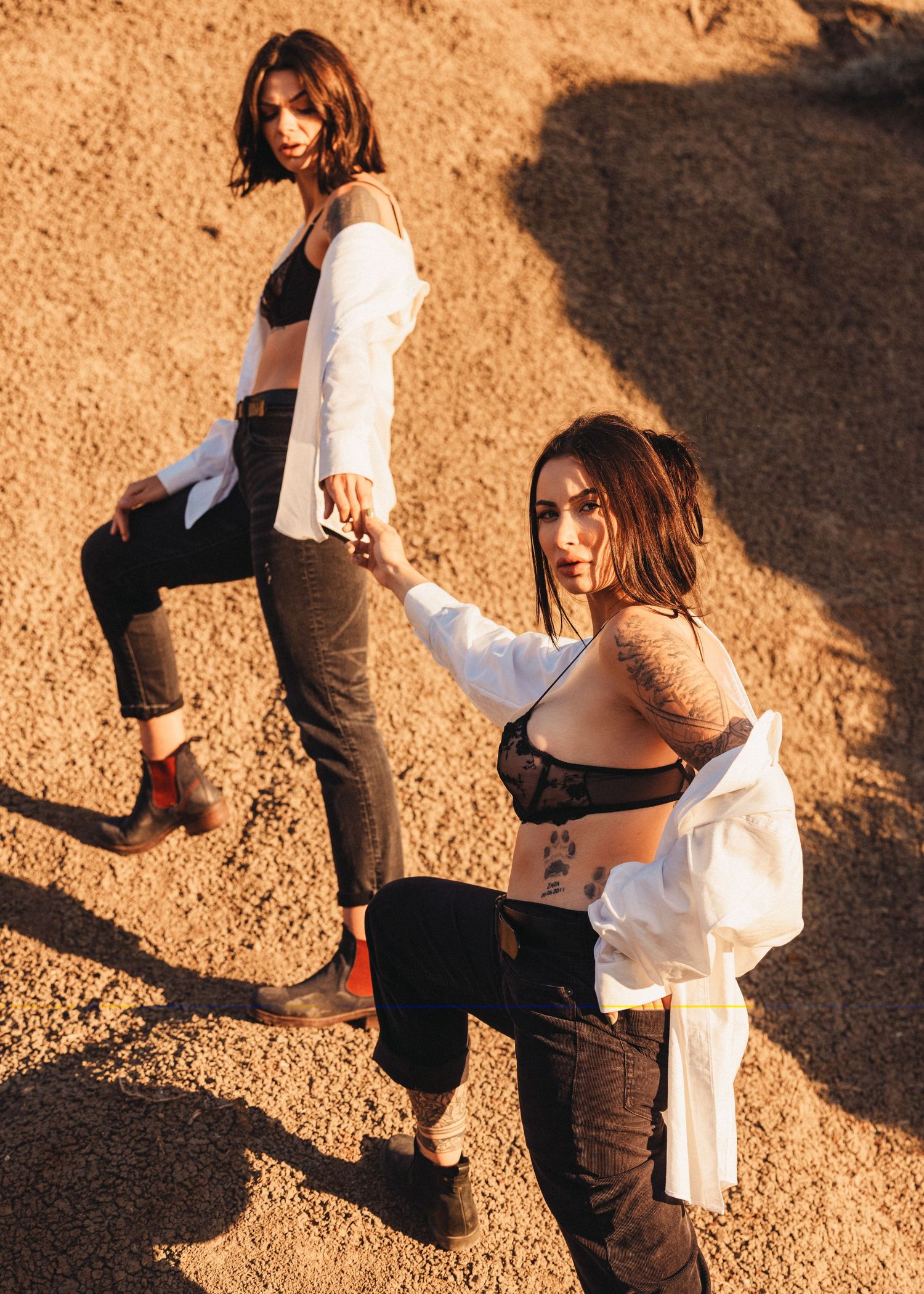 Two people in contrasting outfits dance together on sandy ground at sunset.
