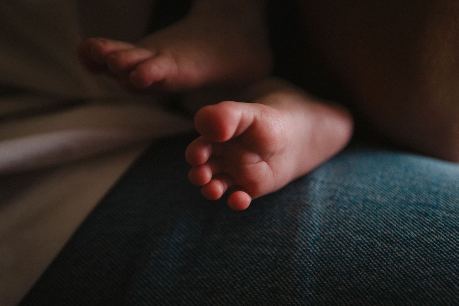 Close-up shot of a tiny baby foot resting on denim fabric.
