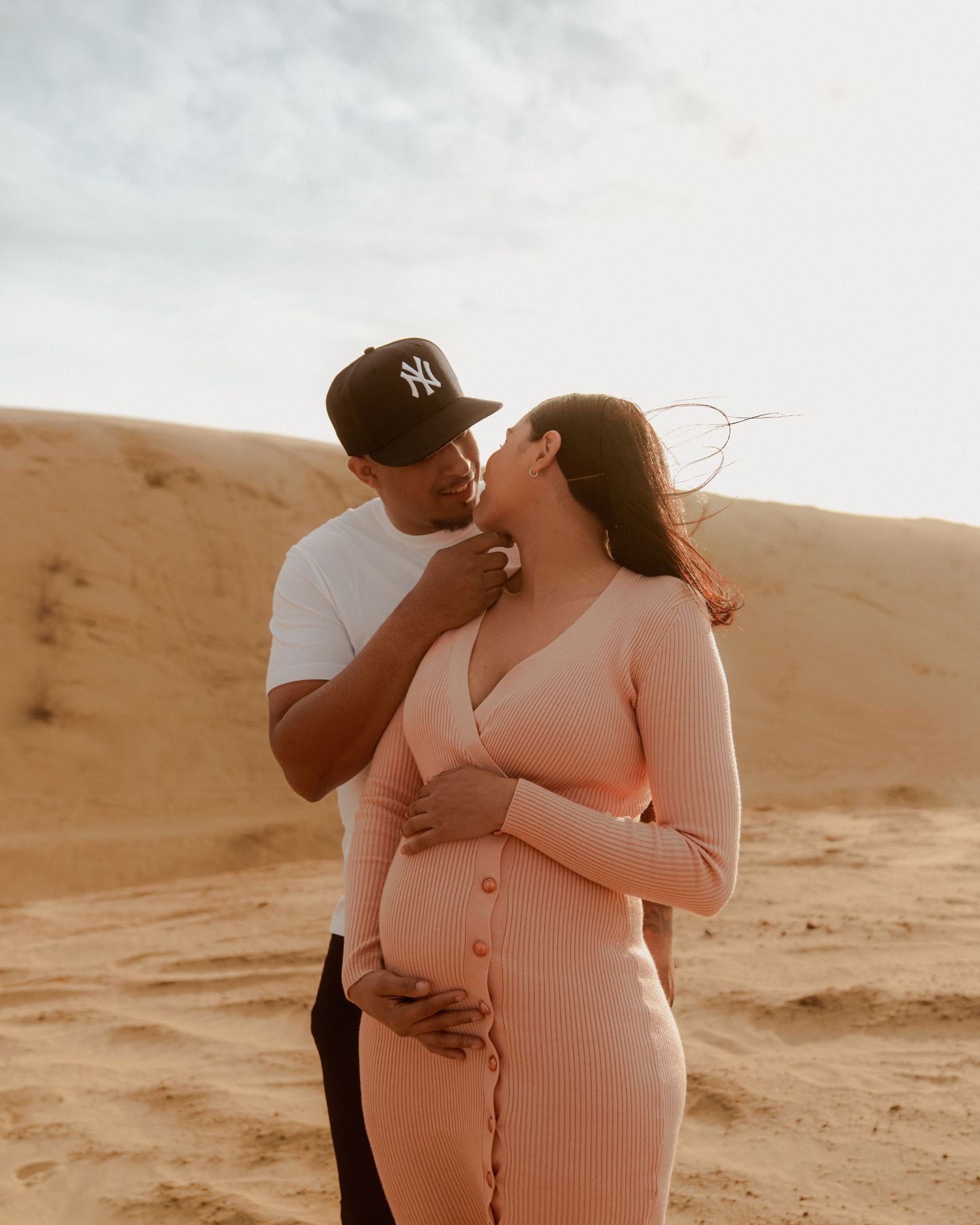 Intimate maternity photoshoot in desert sand dunes at golden hour.