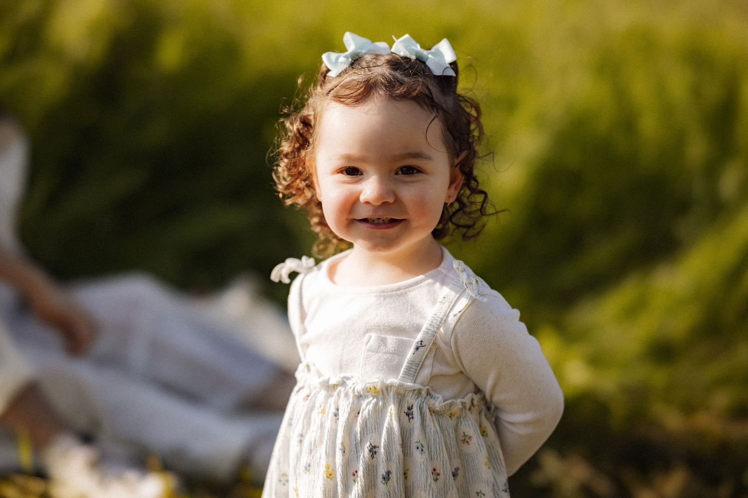 A small child in a white dress smiles while wearing a floral crown.