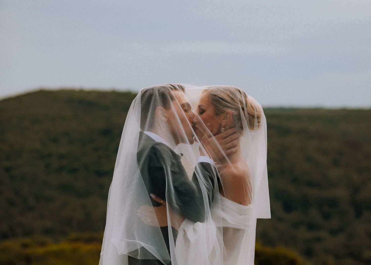 Romantic wedding moment captured through a veil with mountains in background.